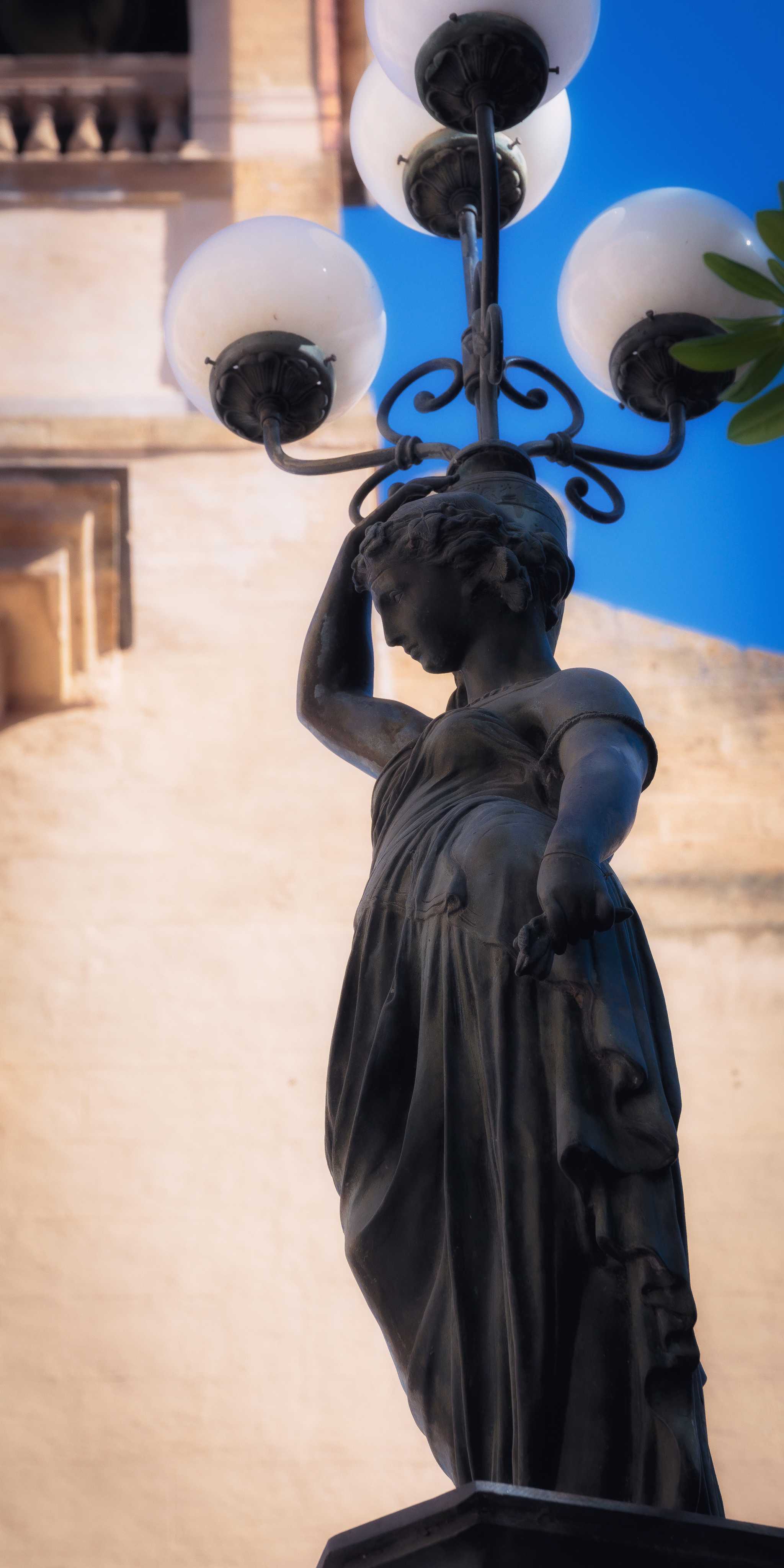 Statue of an ancient woman in front of a lamp post in Corleone.