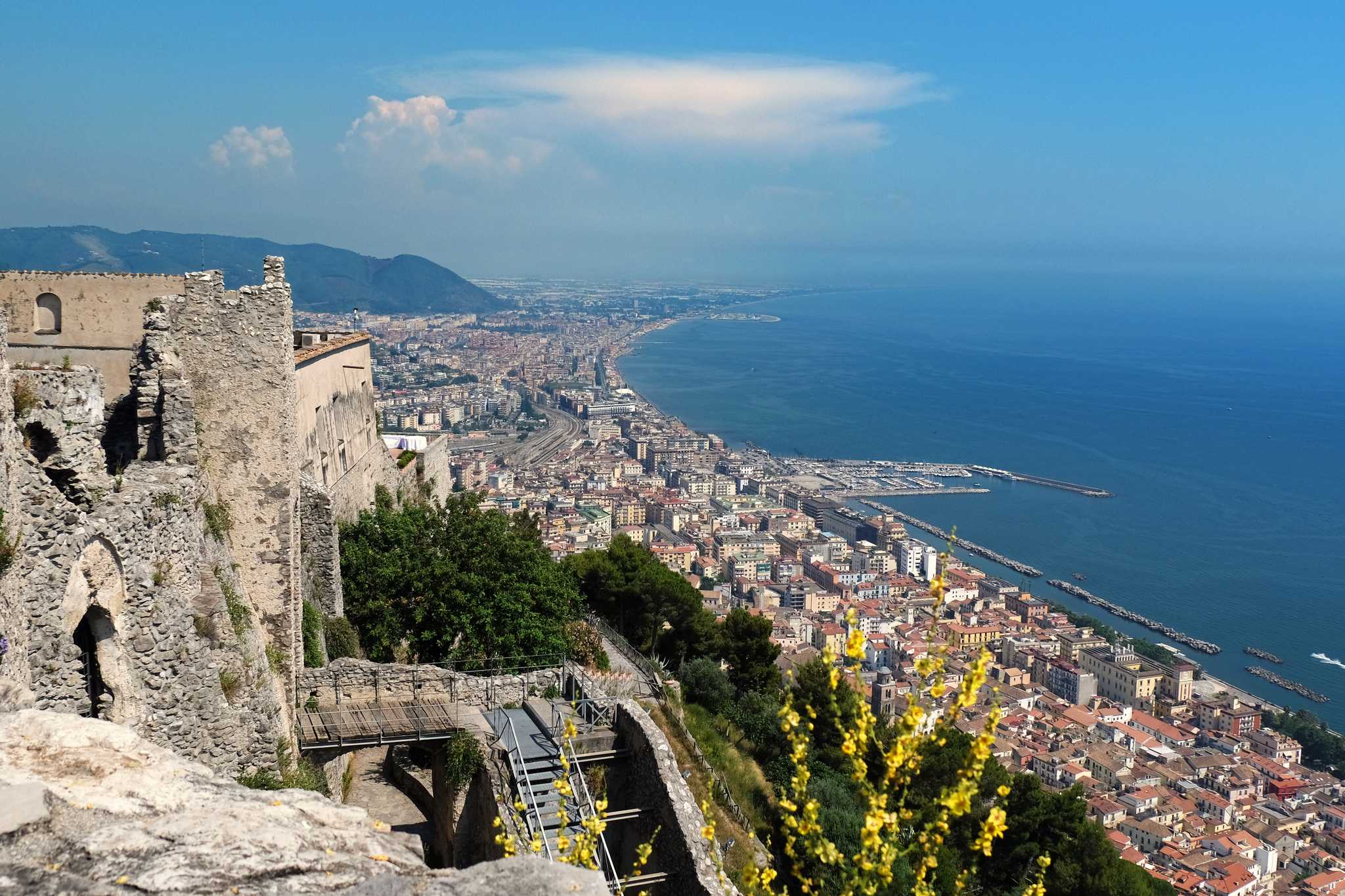 View from Arechi Castle in Salerno, stone ramparts above the city, port, and curving coast.
