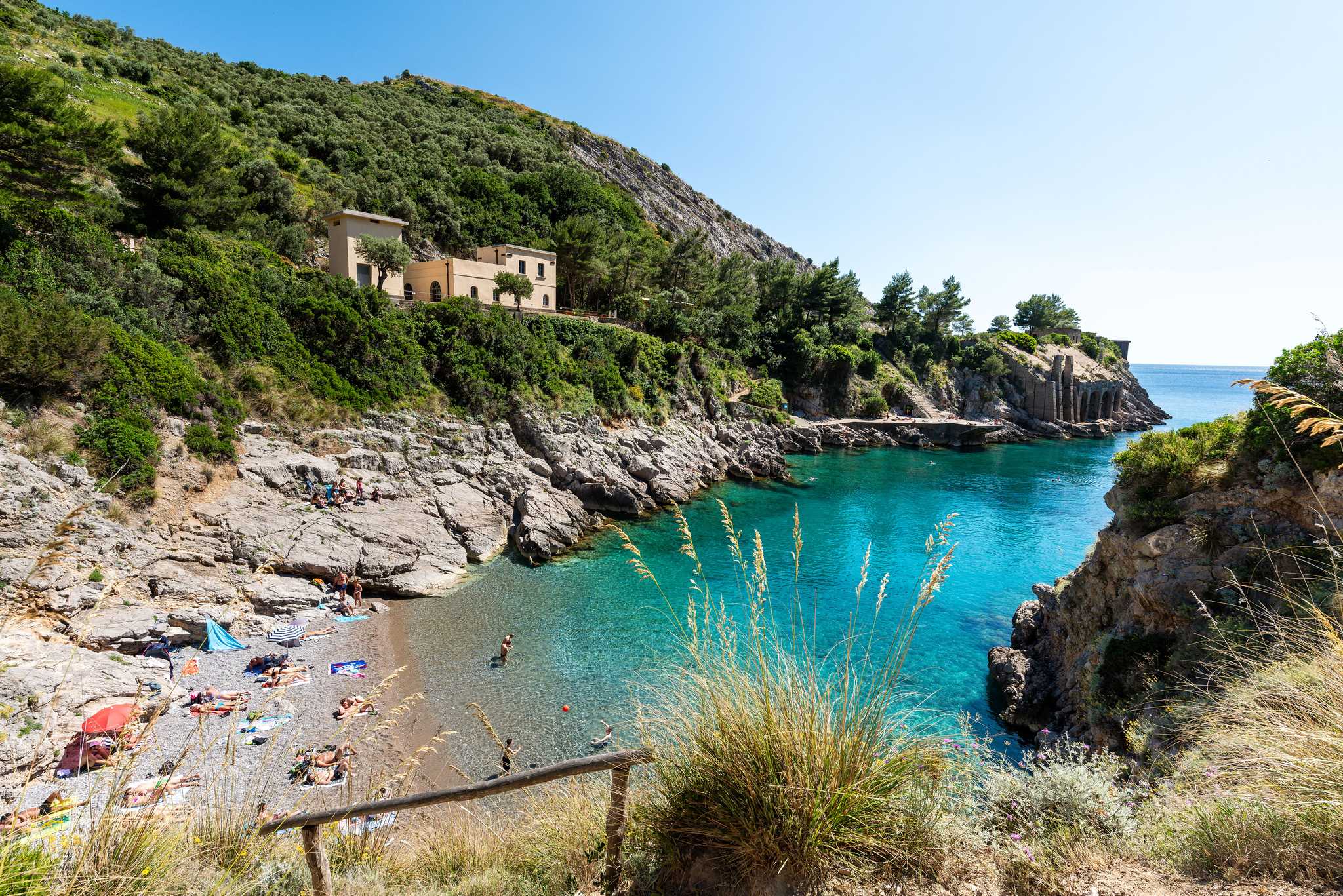 A secluded cove at the Bay of Ieranto on the Sorrento Peninsula, with sunbathers on a small pebble beach.