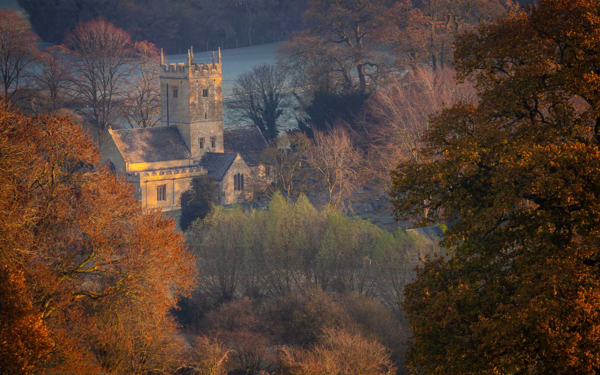A medieval English castle surrounded by trees in shades of green, orange, and red. LP: