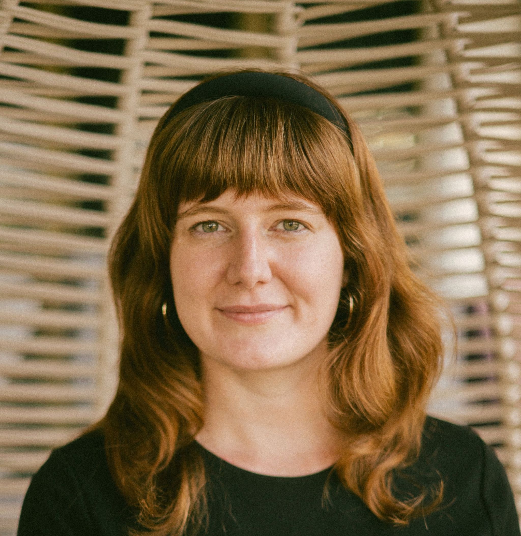 A headshot of a woman in a black dress and headband.
