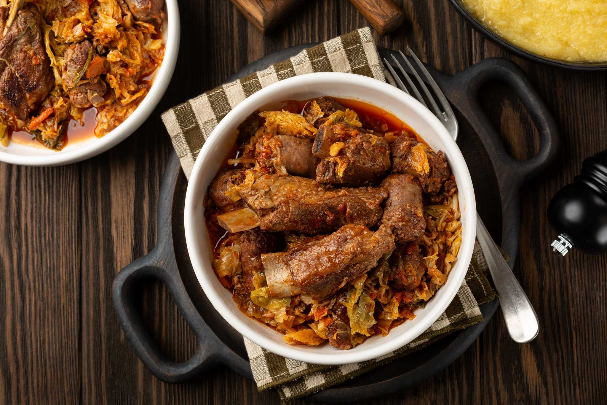 A bowl of hearty meat stew, Cassoeula, on a rustic table with silverware.