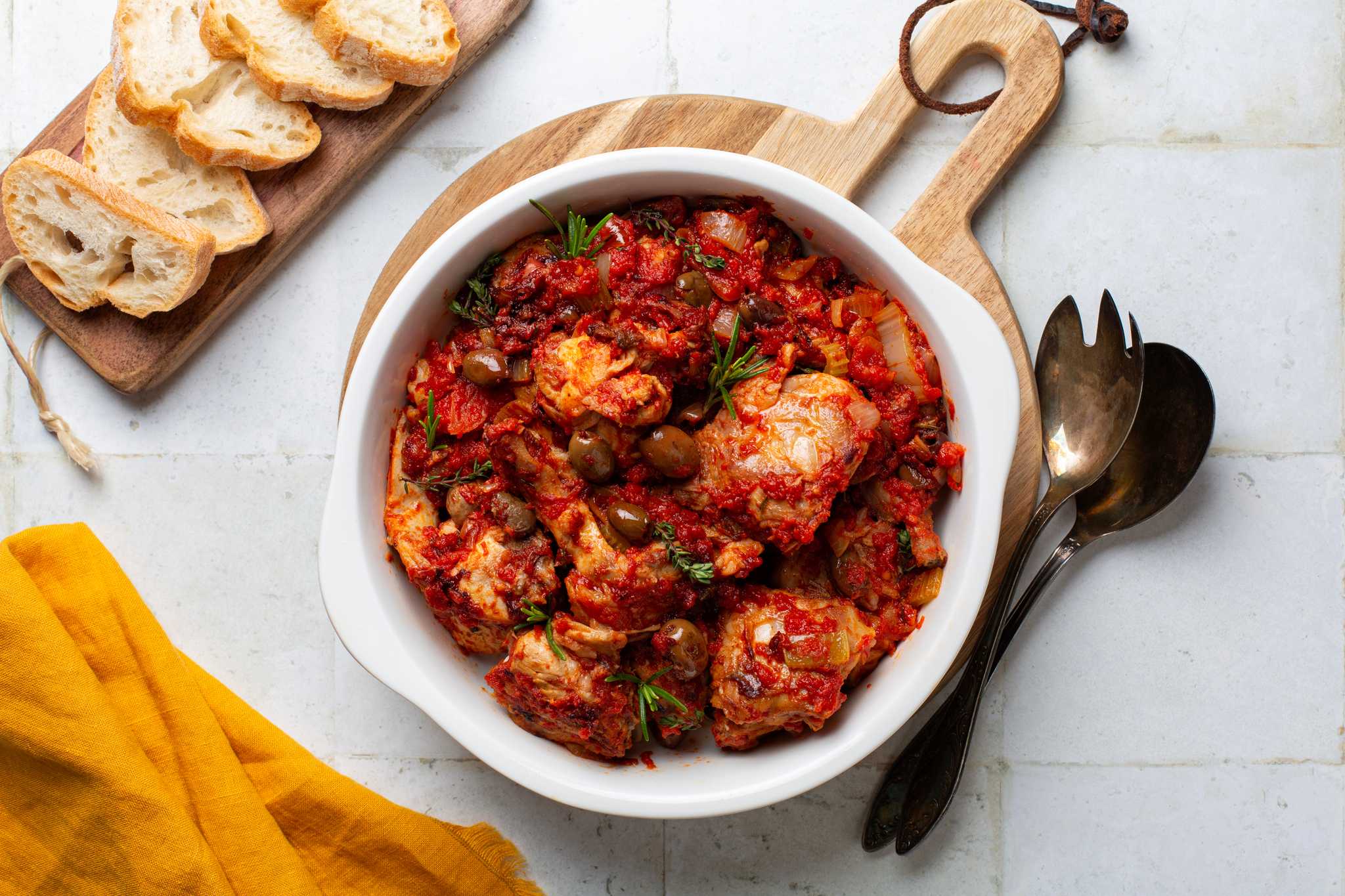 Coniglio all'ischitana, bone-in rabbit braised in tomato with olives and herbs, in a white dish.