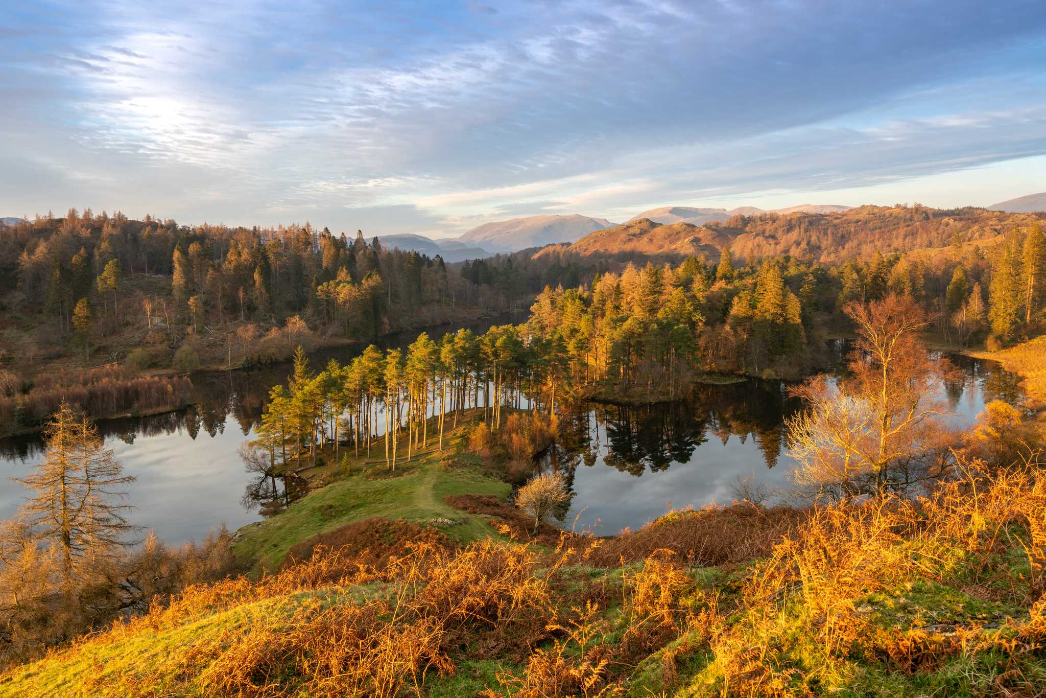 A small lake sits in the foreground as forested hills stretch all the way to the horizon.