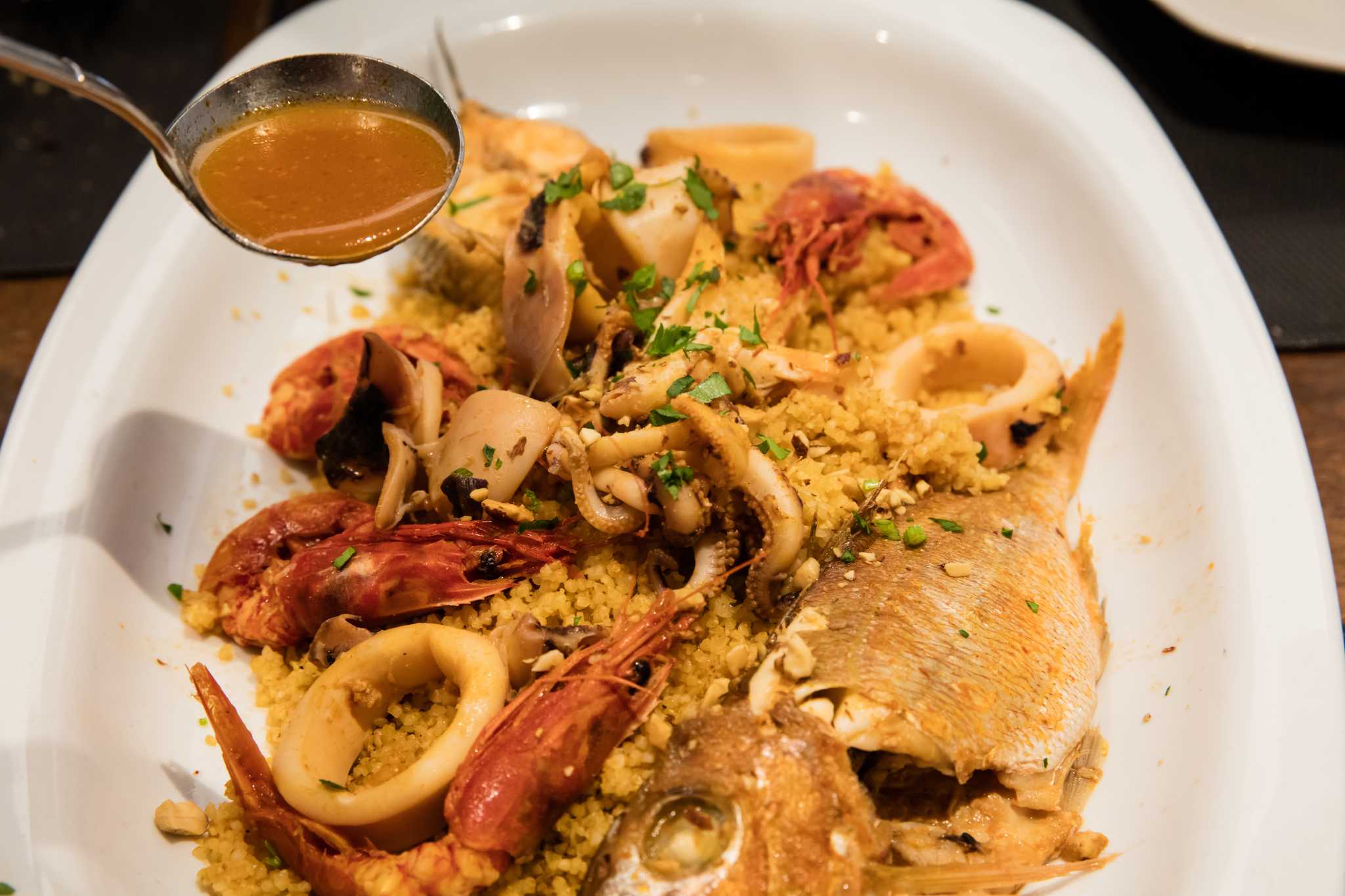 Trapani-style fish couscous with prawns, squid, and whole fish, broth ladled over the top.