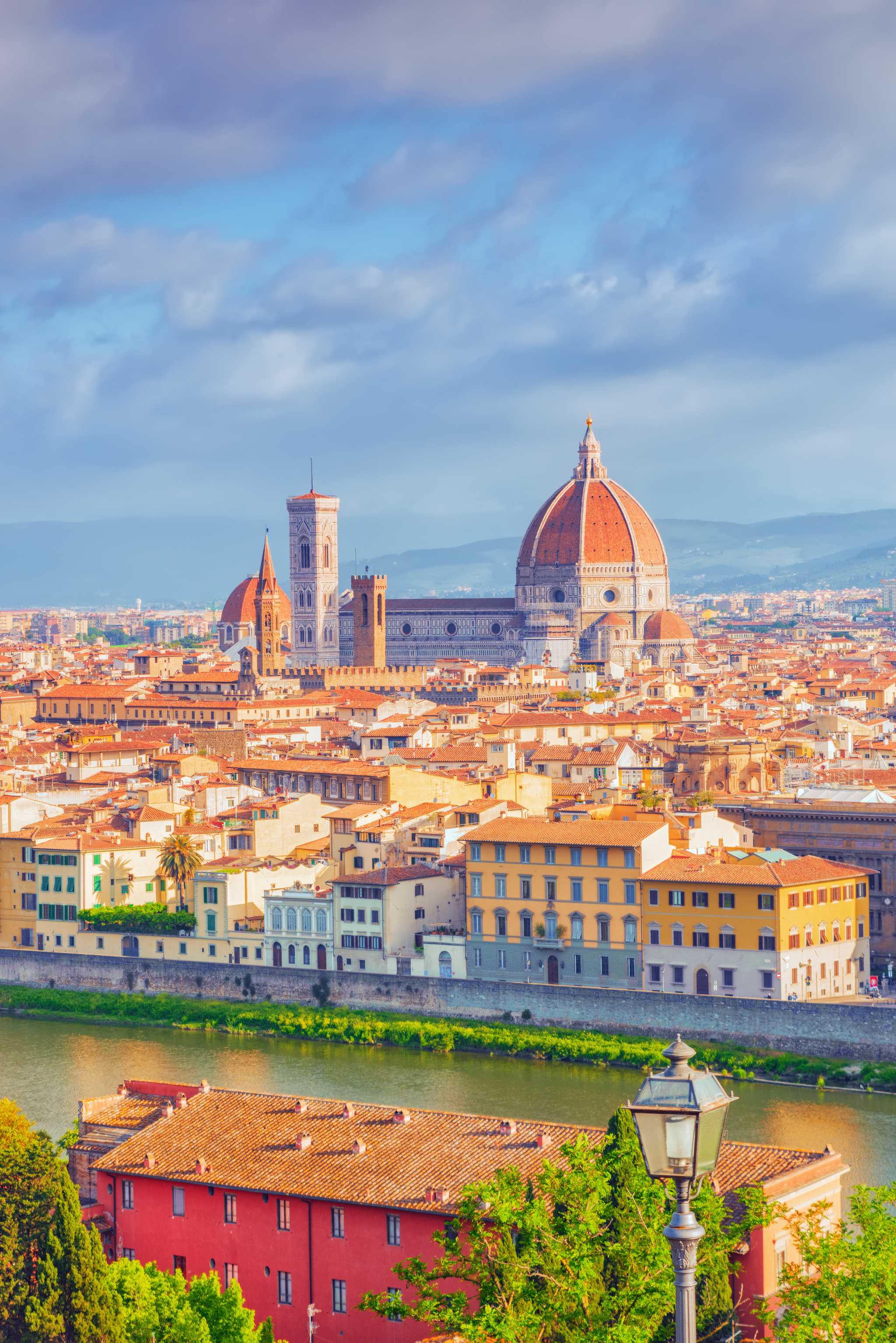 A view over Florence, the Duomo's red dome and marble bell tower above the rooftops and the Arno River.