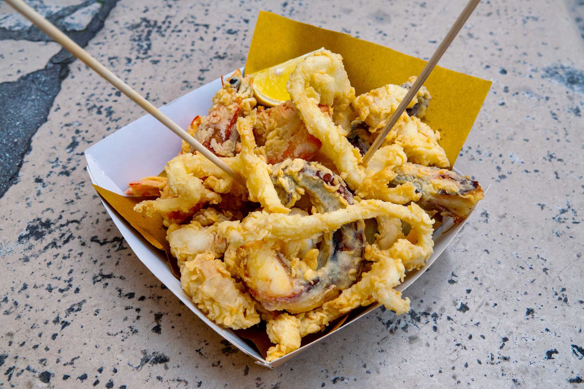 A white paper takeaway boat filled with golden battered fried seafood.
