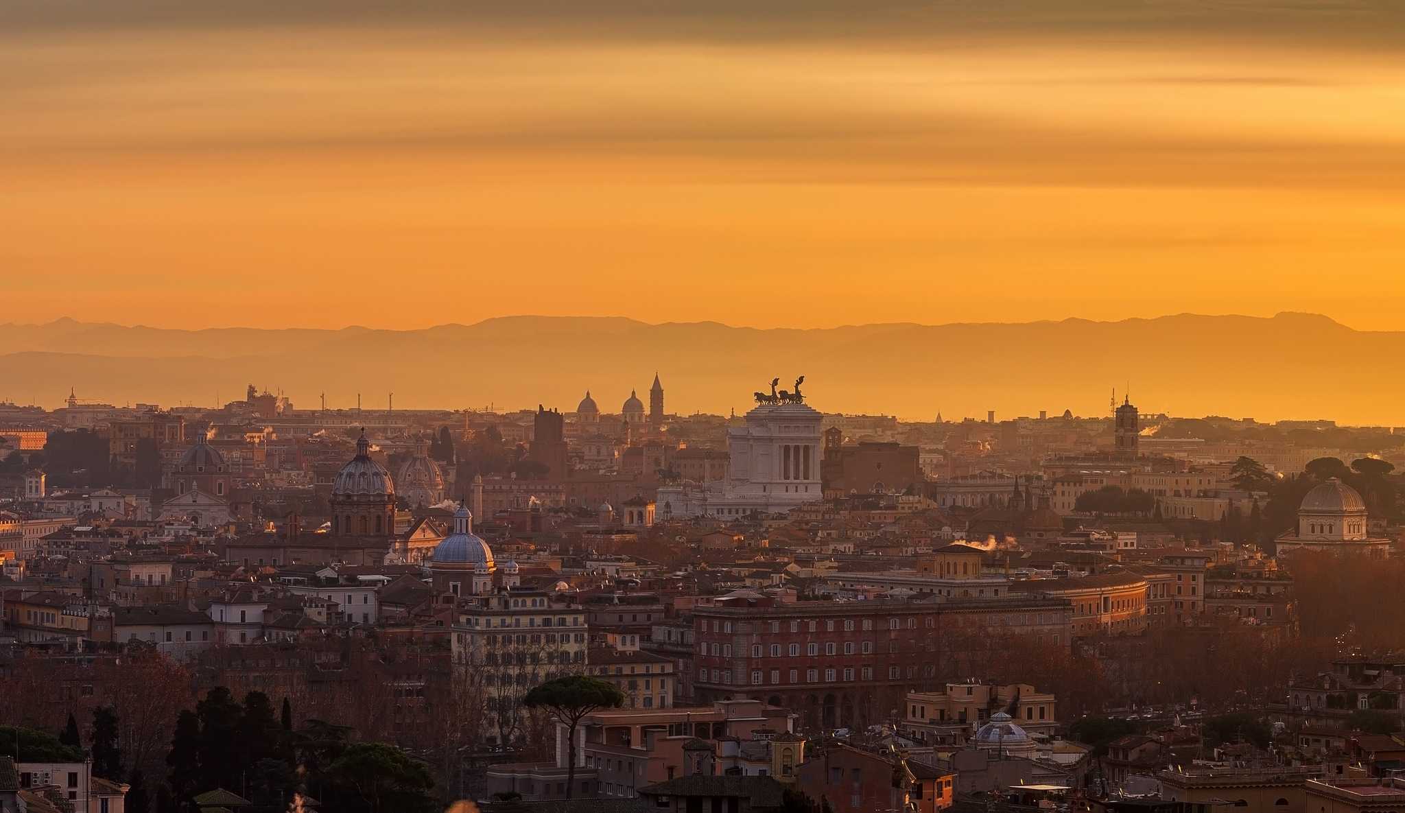 Rome's domes and rooftops under an orange sunset sky, seen from the Gianicolo.