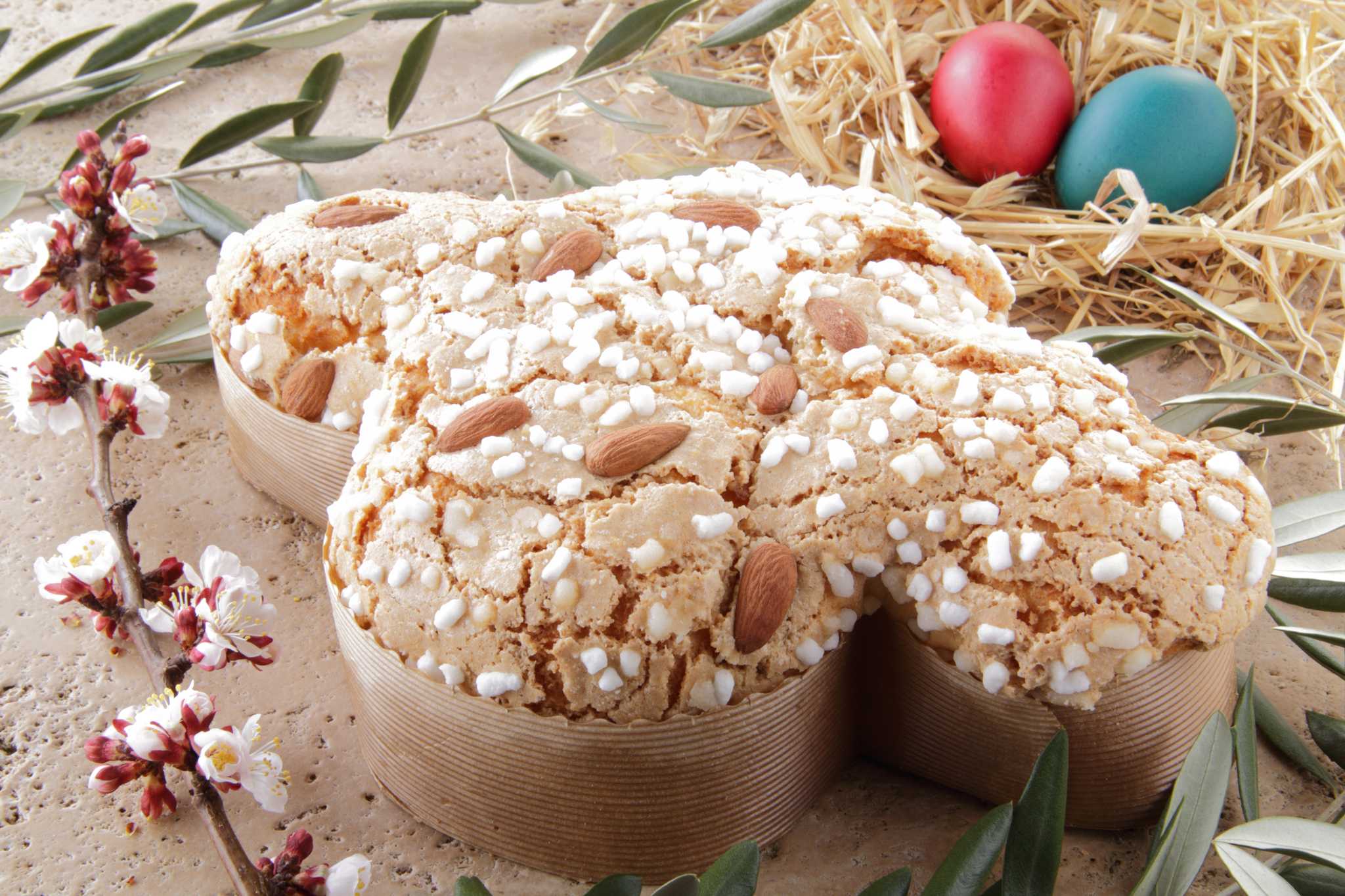 Colomba di Pasqua with almonds and sugar beside dyed Easter eggs and blossoms.