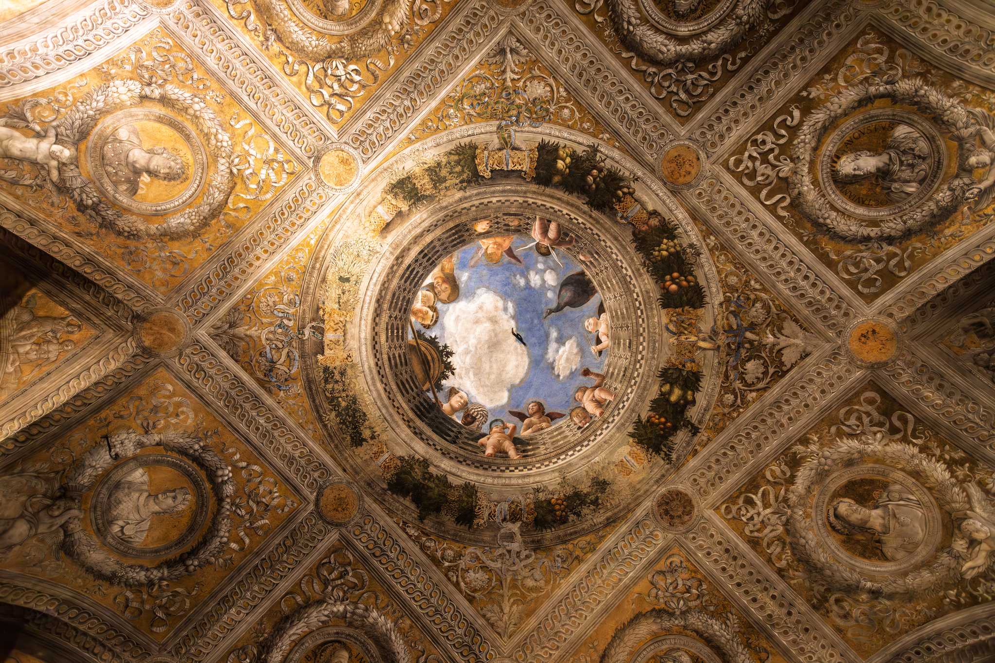 A painted ceiling in Mantua's Camera degli Sposi with cherubs looking down from a ring of blue sky.