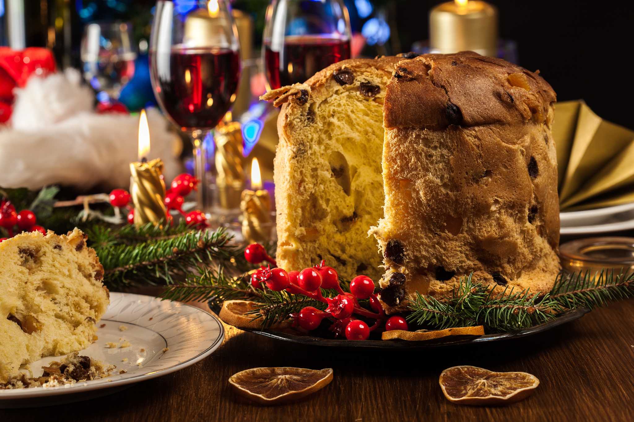 Sliced panettone on a festive table with candles, berries and red wine.