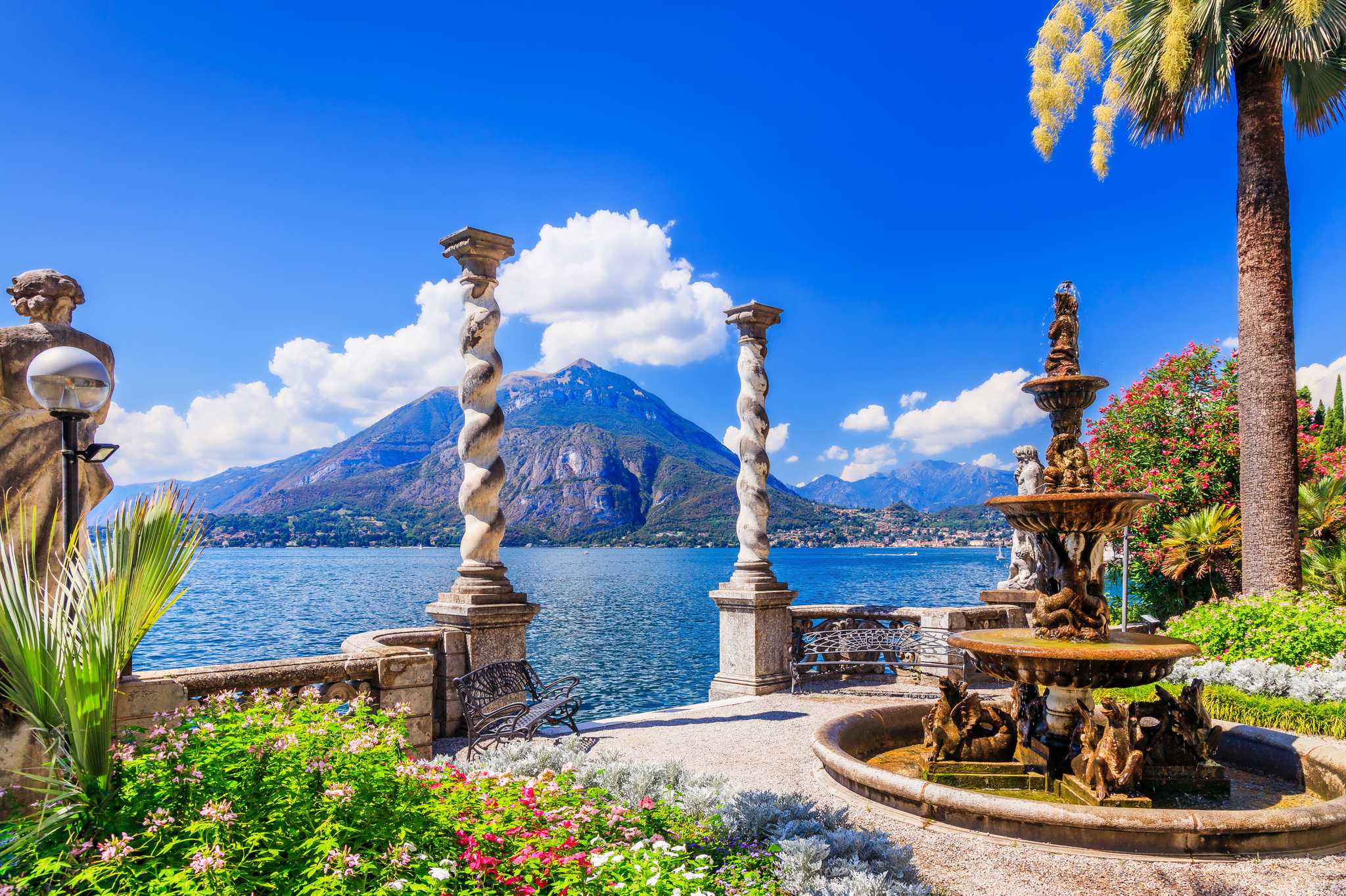 Twisted marble columns and a fountain in a lakeside garden above Lake Como, with mountains across the water.