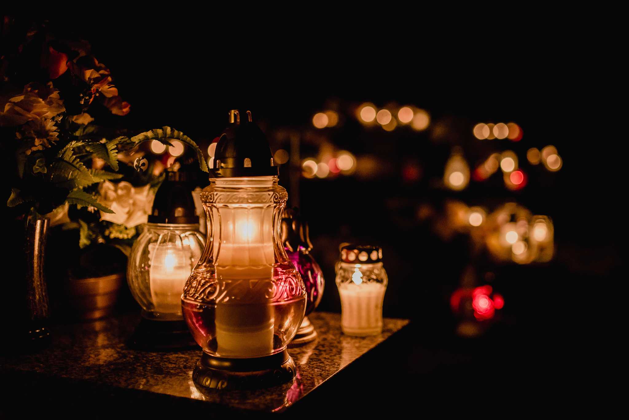 Votive candles and flowers glowing on graves for All Saints' Day at night.