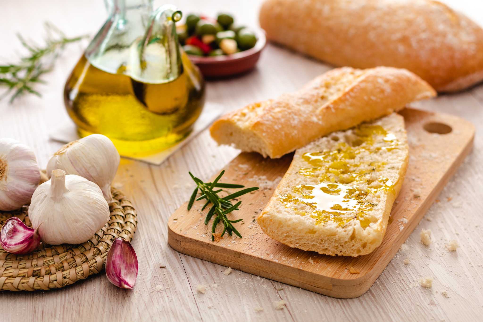 Bread drizzled with new olive oil beside garlic, rosemary and a glass cruet.