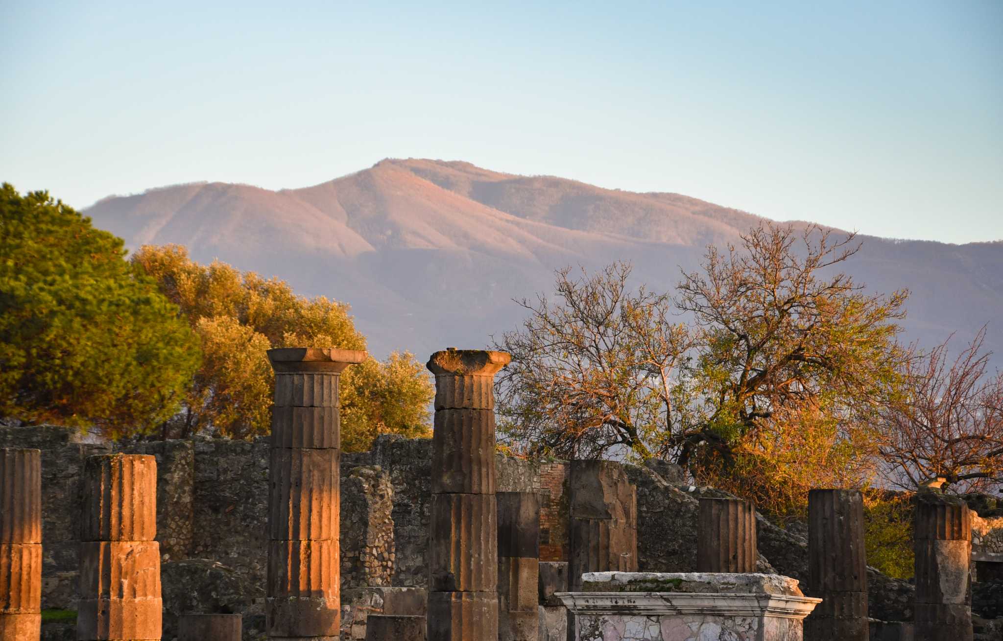 Ancient columns and ruins at Pompeii below a mountain in late autumn light.