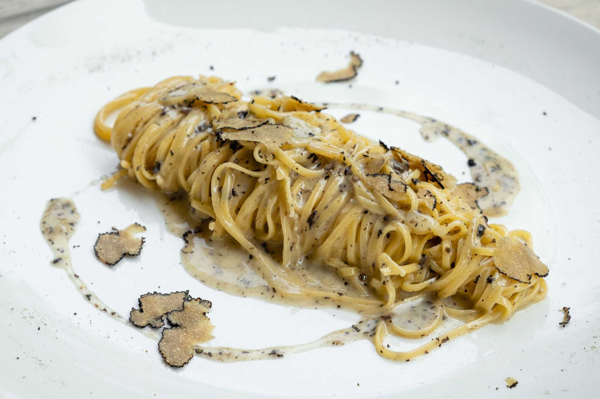 Tajarin pasta in creamy sauce topped with shaved black truffle on a white plate.