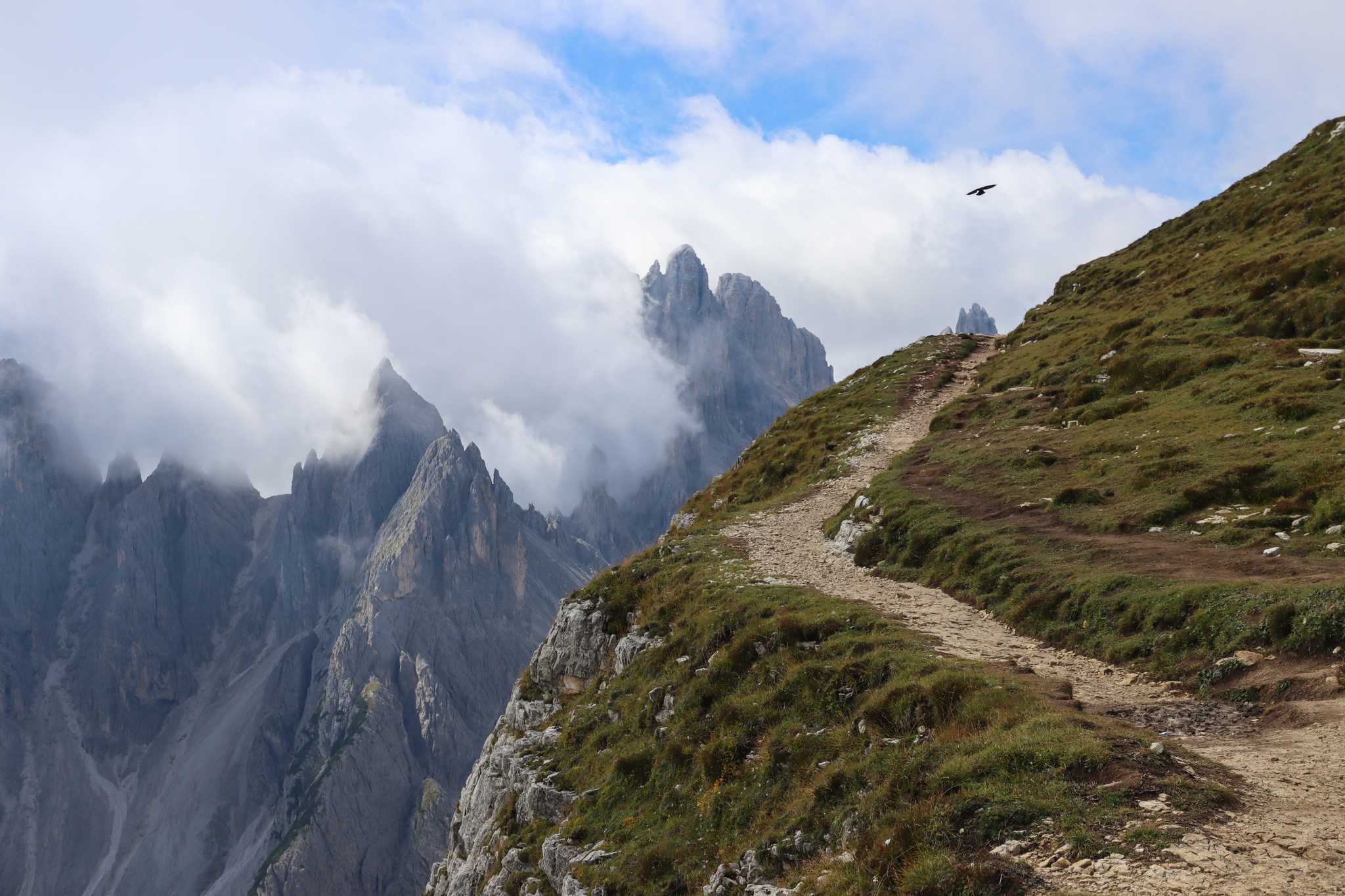 Hiking trail along a ridge with cloud-wrapped Dolomite peaks in the distance.