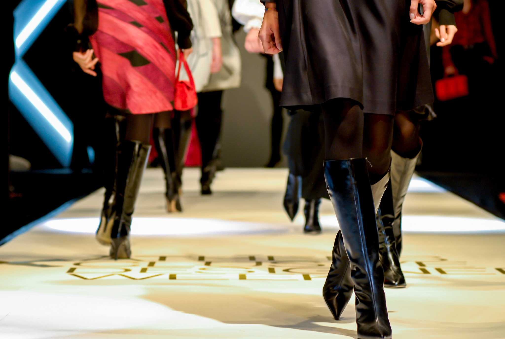 Models in tall boots walk the runway at a fashion week show.