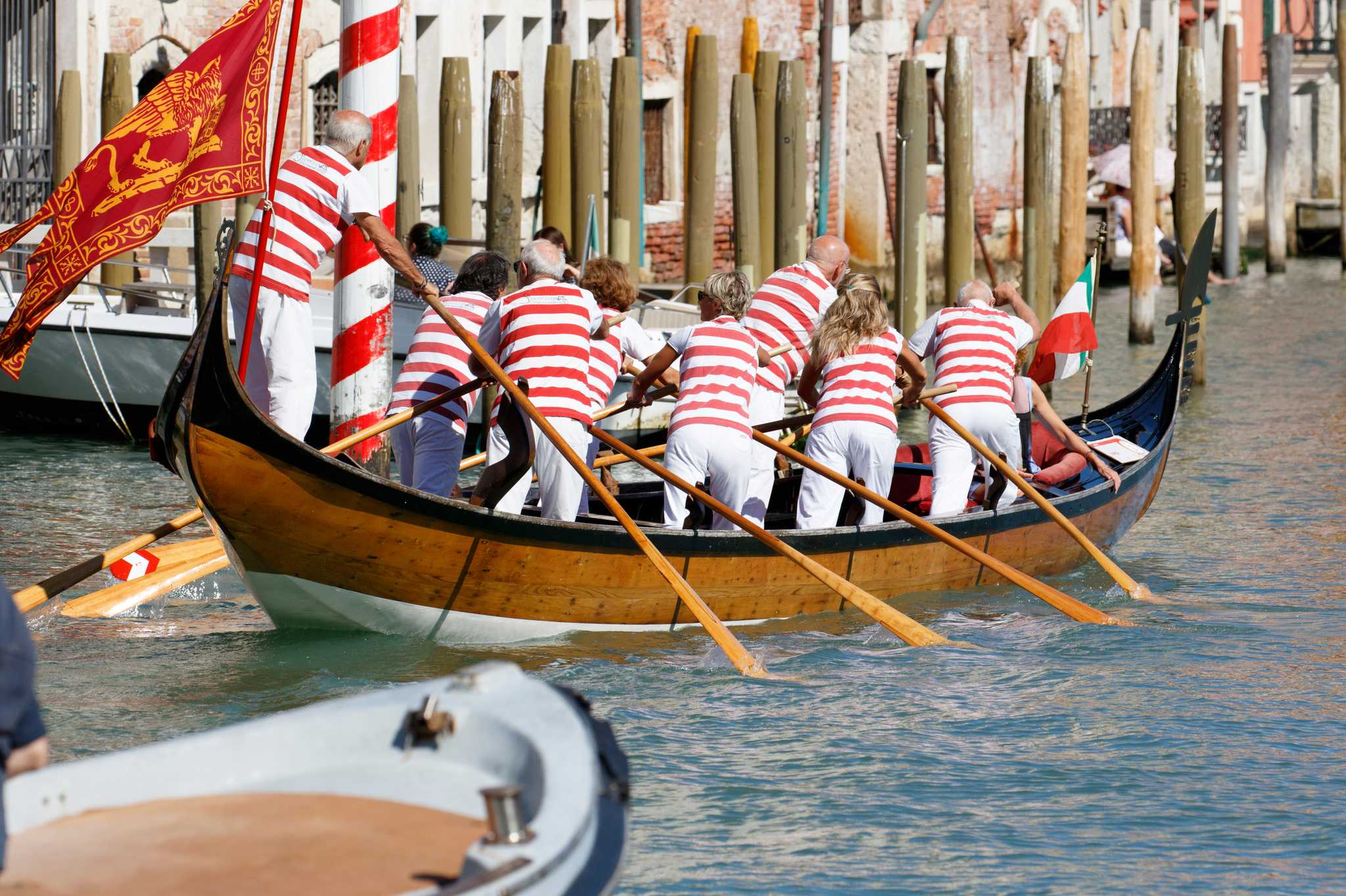 Rowers in striped shirts race a wooden boat at the Regata Storica in Venice.