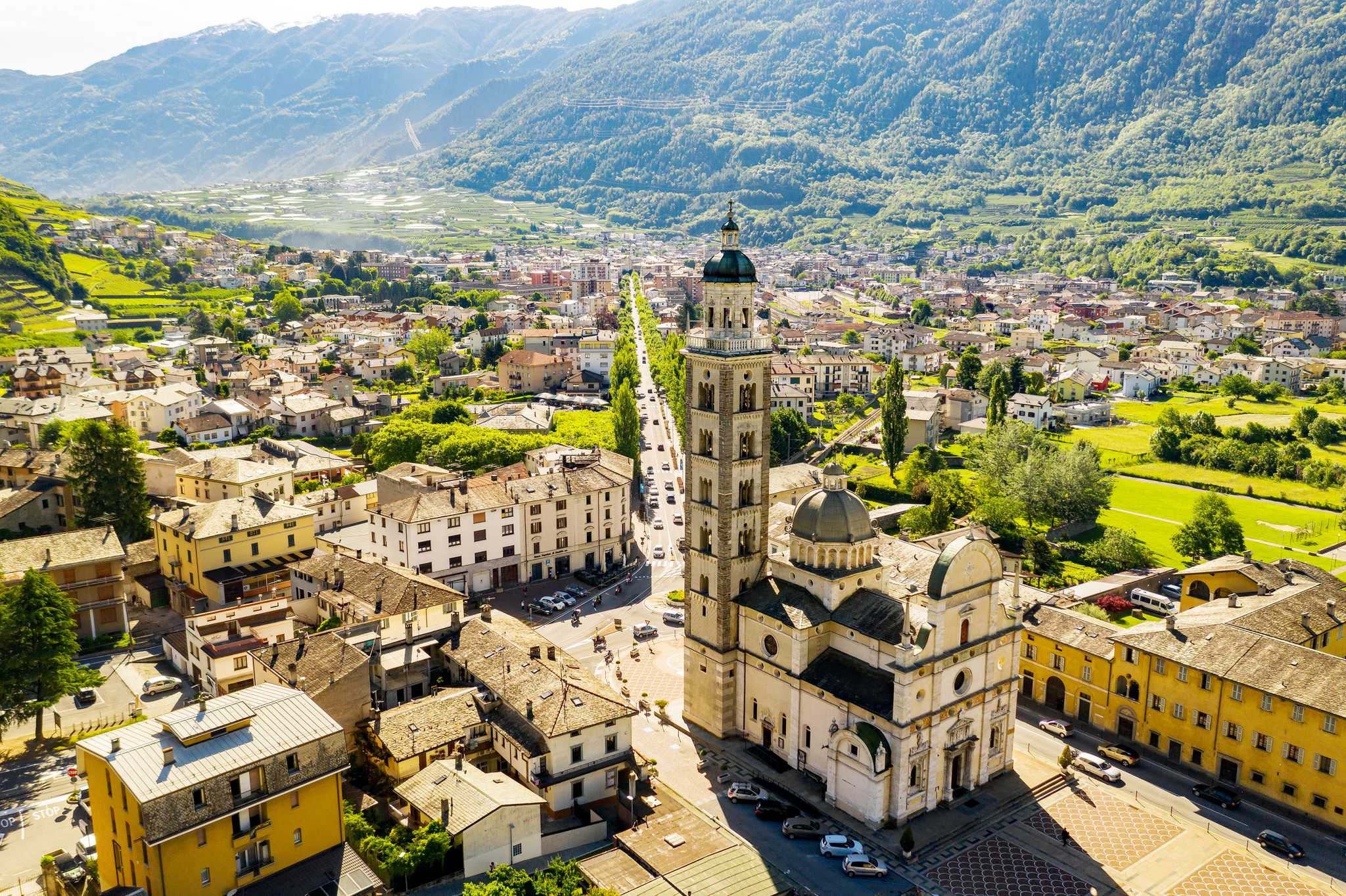 The town of Tirano sitting in a valley of green mountains, the Basilica of the Madonna di Tirano rising above it.