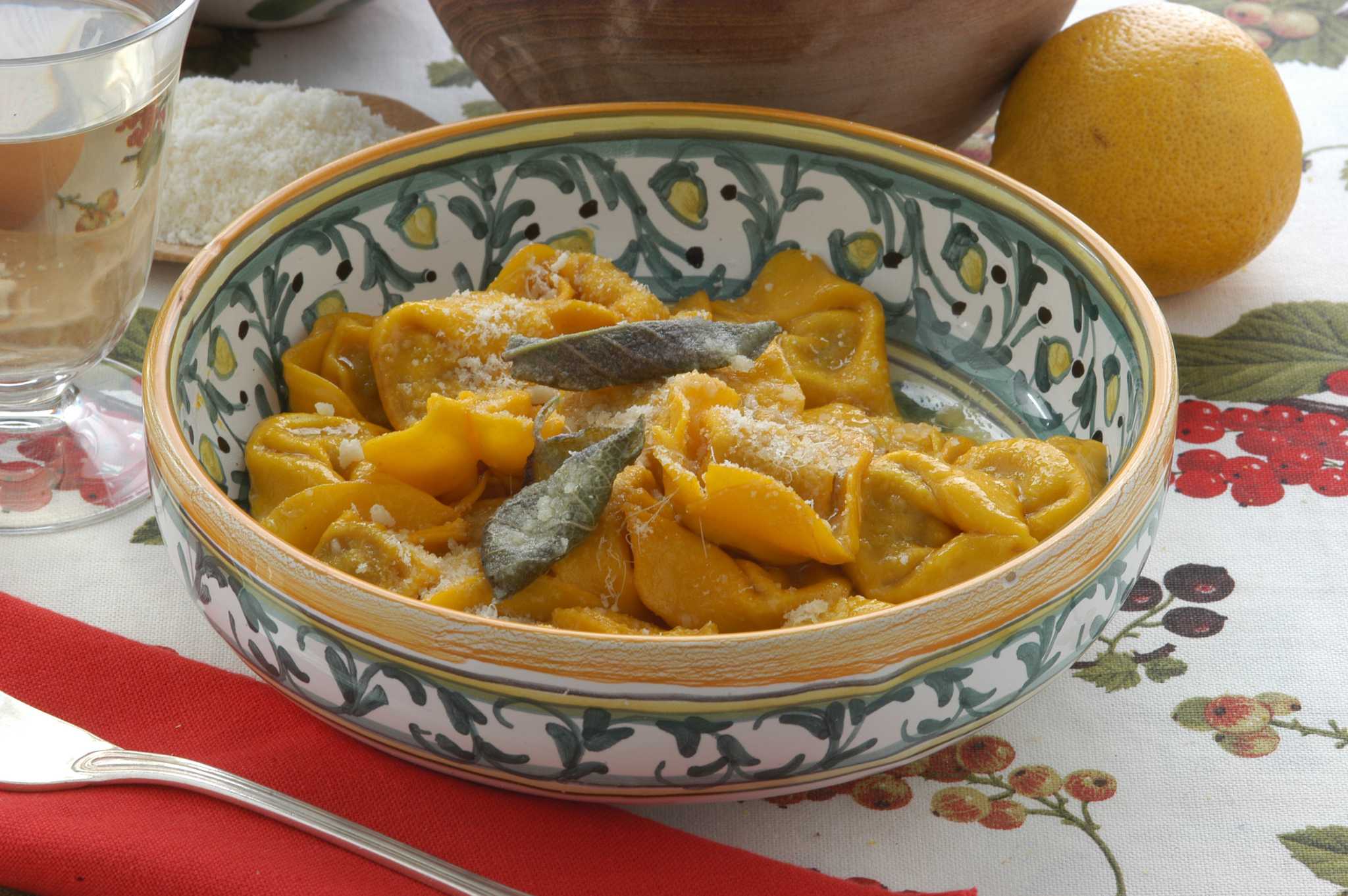 Stuffed pasta parcels topped with herb leaves and grated cheese in a painted ceramic bowl.