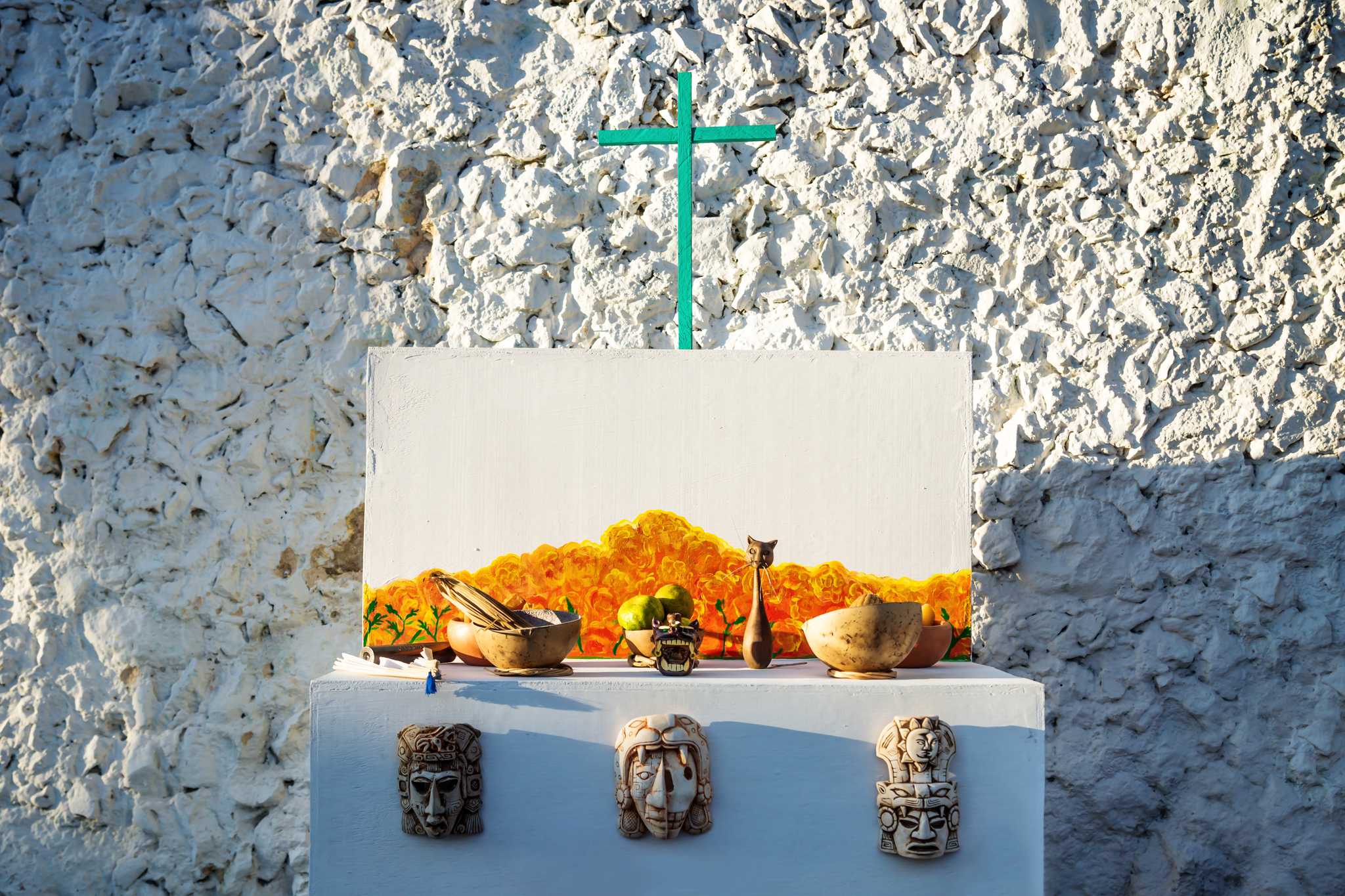A man with his head bowed, surrounded by candles in a graveyard for Day of the Dead.