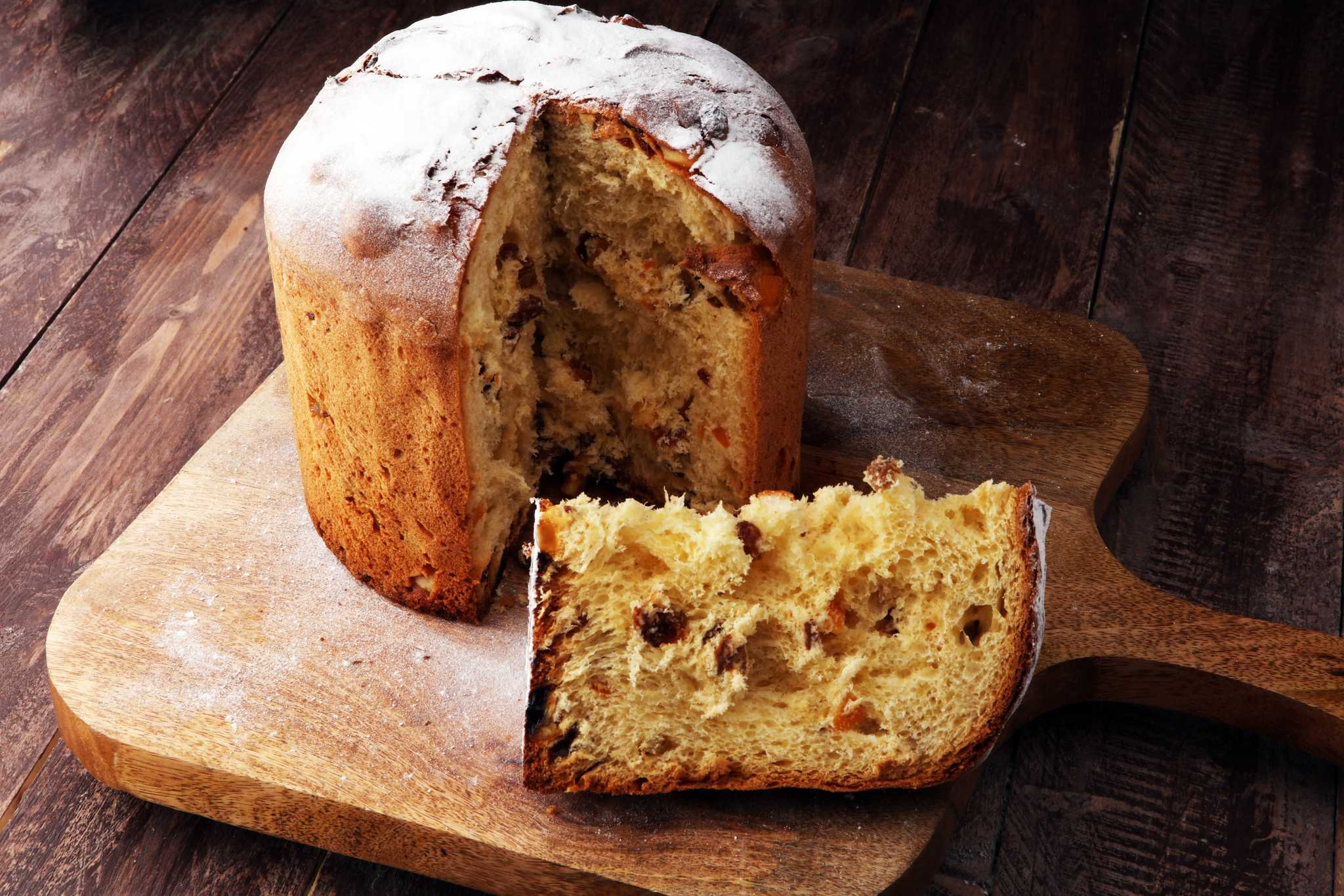 Christmas Panettone cake on a wooden cutting board with one slice cut out.