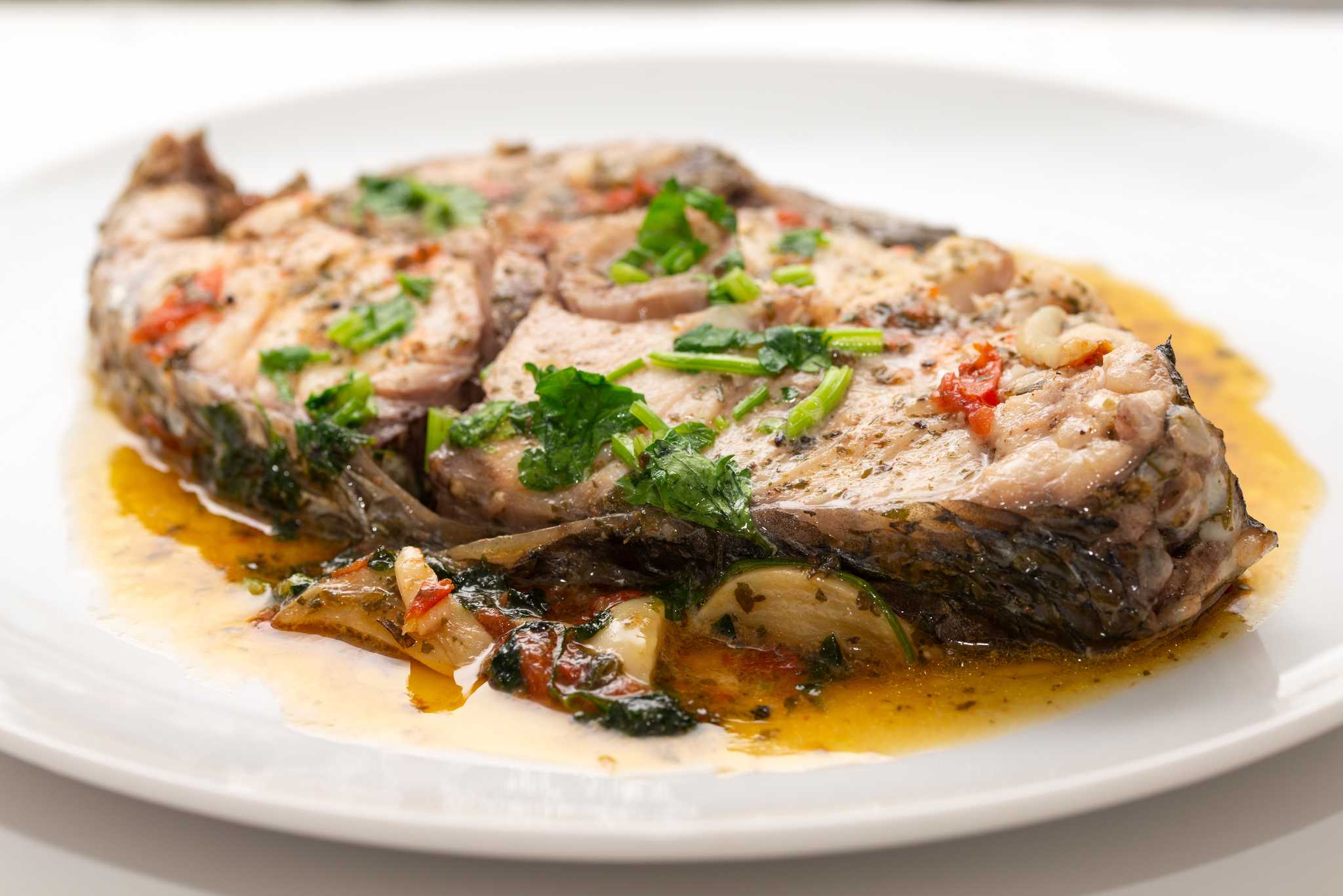 A close-up of pesce all'acqua pazza, a fish steak poached in a light golden broth.