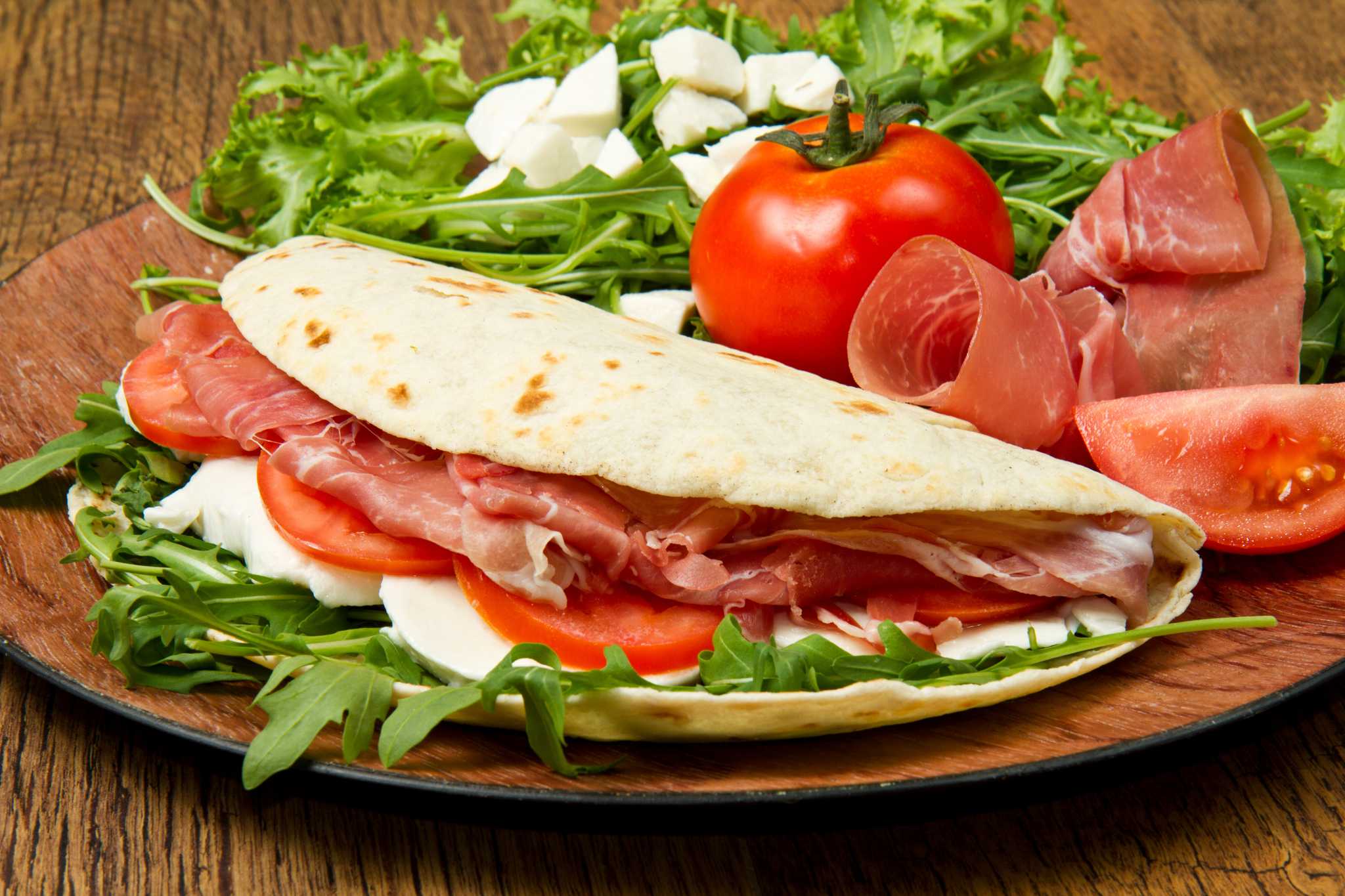 Piadina, an Emilia-Romagna flatbread sandwich, on a plate with salad and tomato.