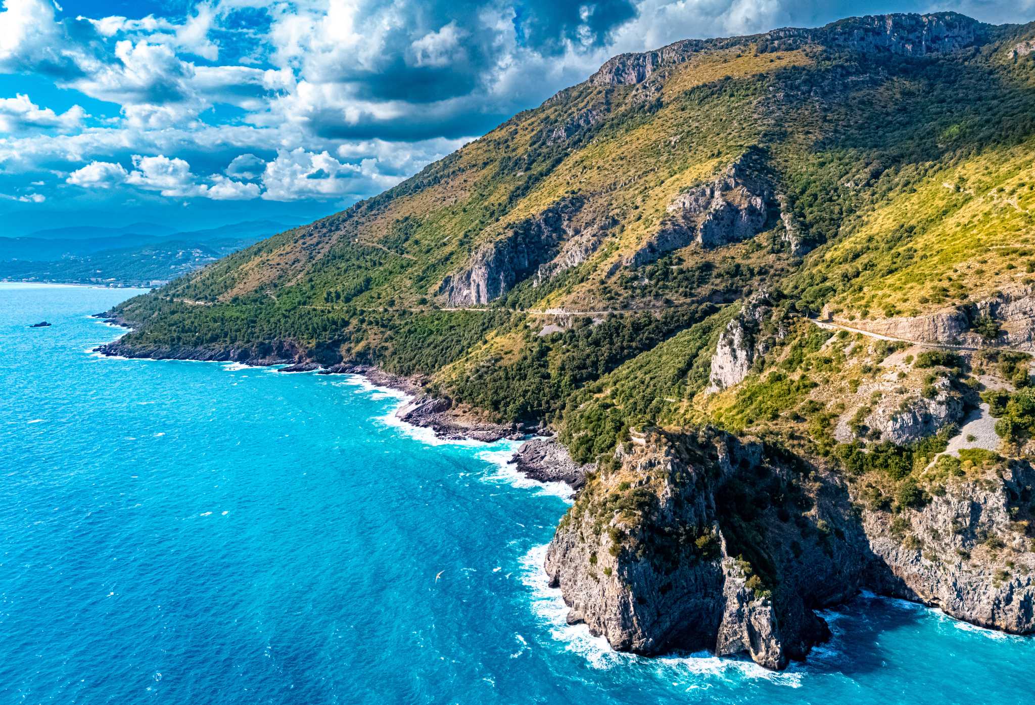 Green cliffs and a winding coast road above bright turquoise sea.