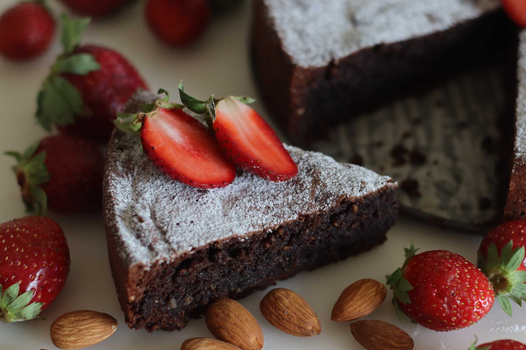 Slice of torta caprese, flourless chocolate-almond cake with powdered sugar and strawberries.