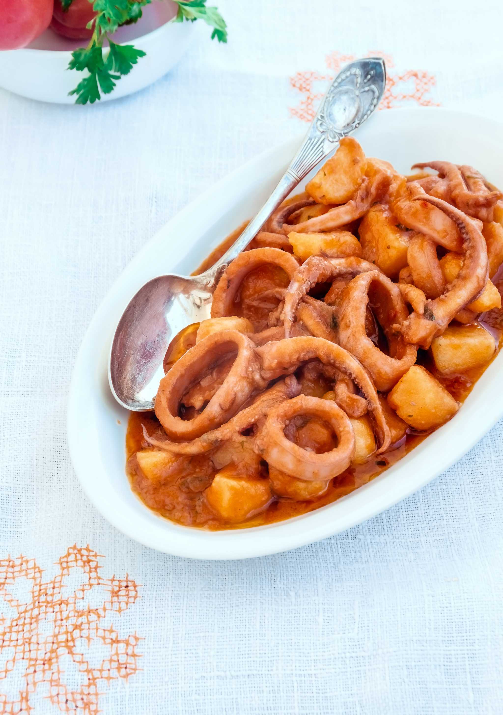 A white oval dish of totani e patate, with squid rings, tentacles, and potatoes.