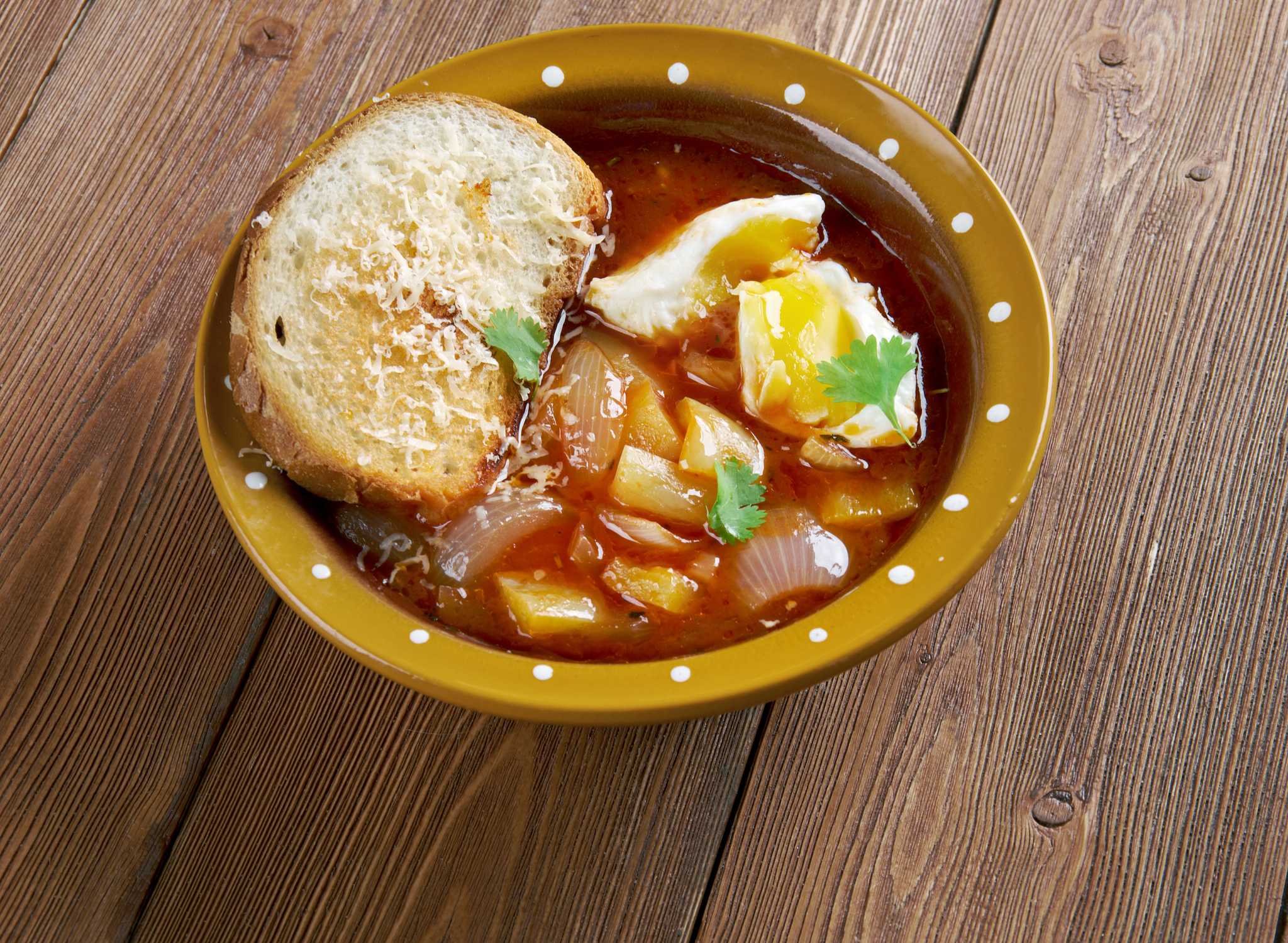Rustic vegetable soup with a poached egg and cheesy toast on a wooden countertop.