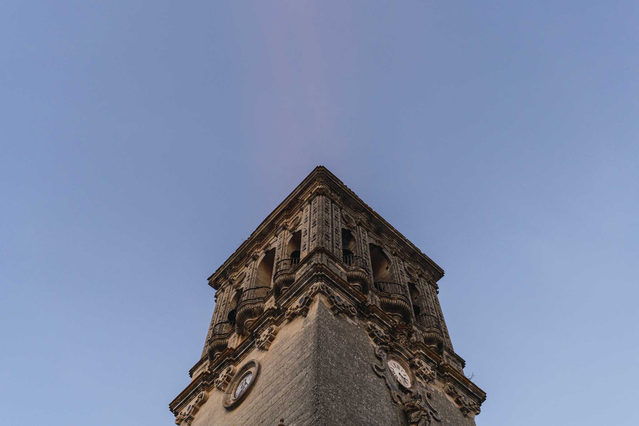 Upward view of an ornate stone bell tower against a clear blue sky.