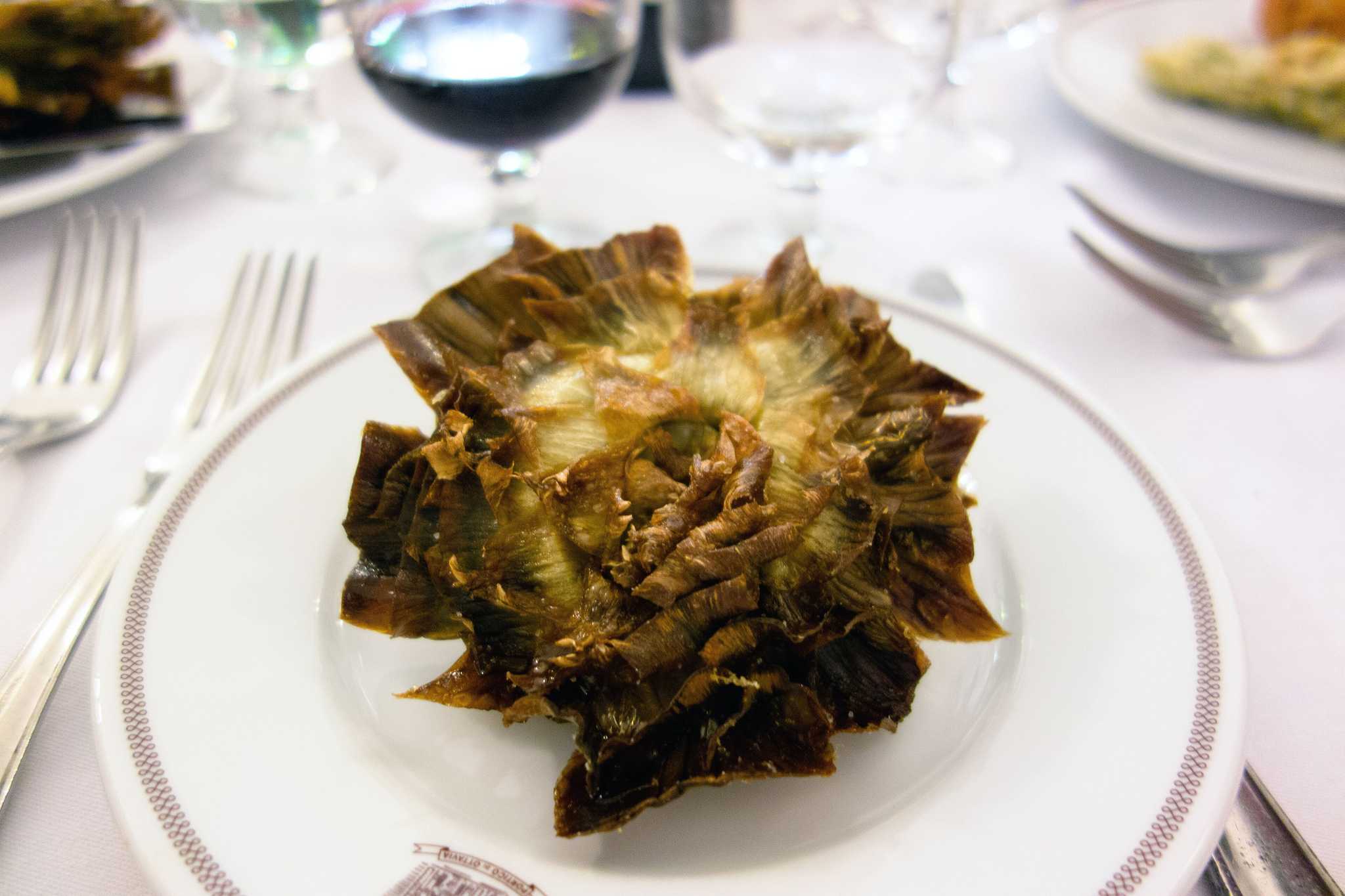 A carciofi alla giudia, or Italian fried artichoke, on a plate on a white tablecloth.