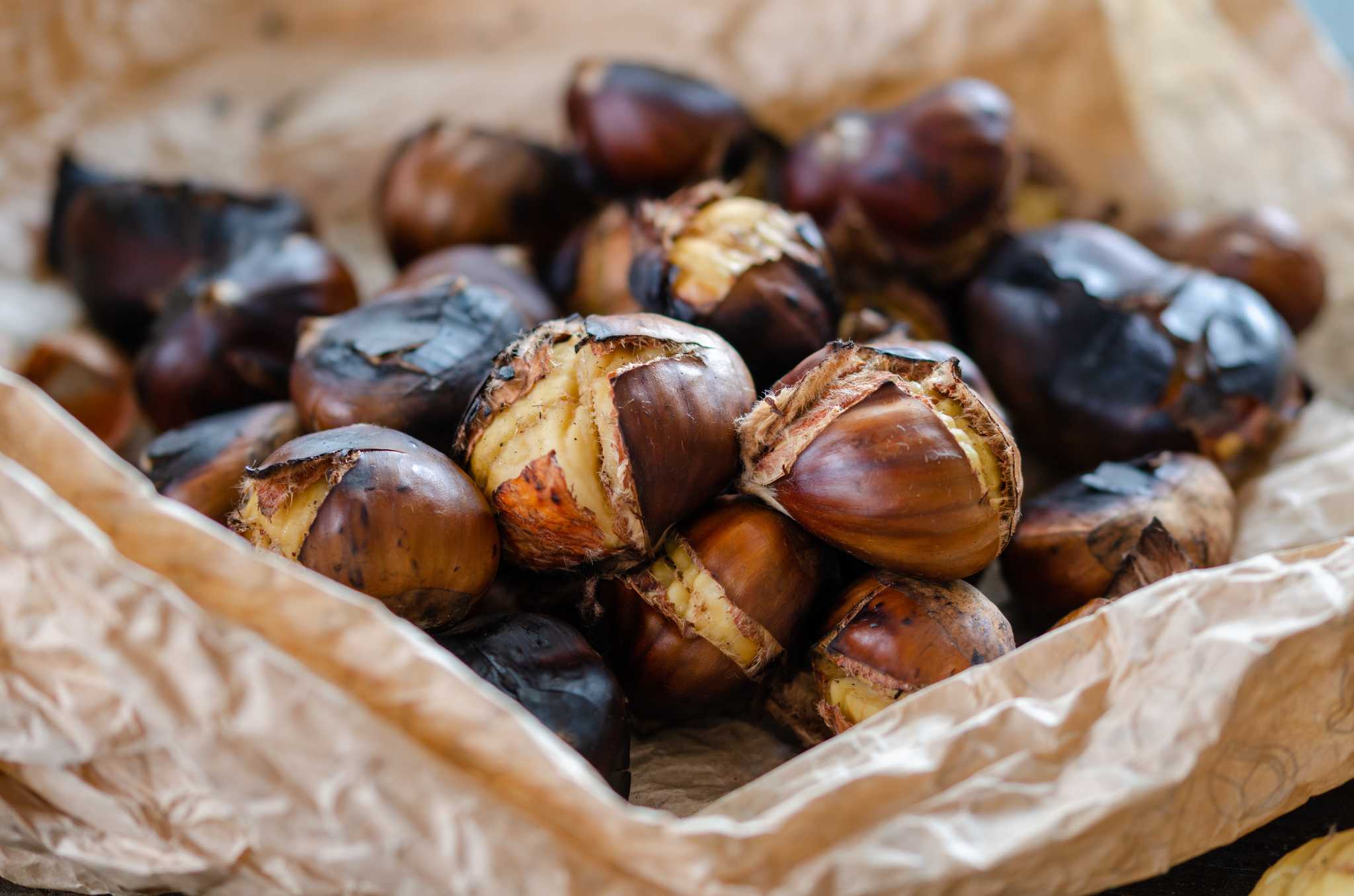 Roasted chestnuts in a brown paper bag, some splitting open.
