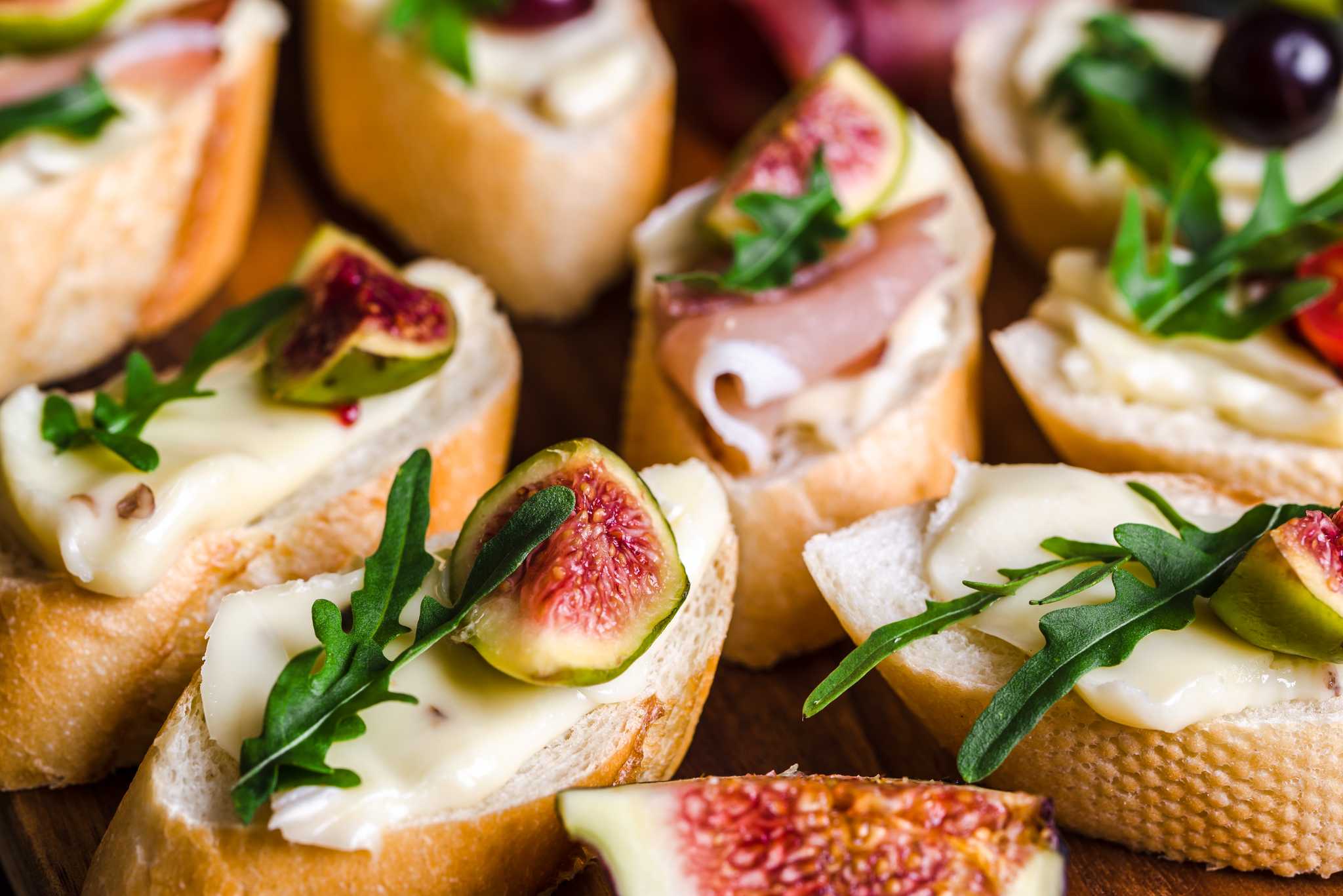 Sliced figs on top of bread with cheese, sliced meat, and greens.