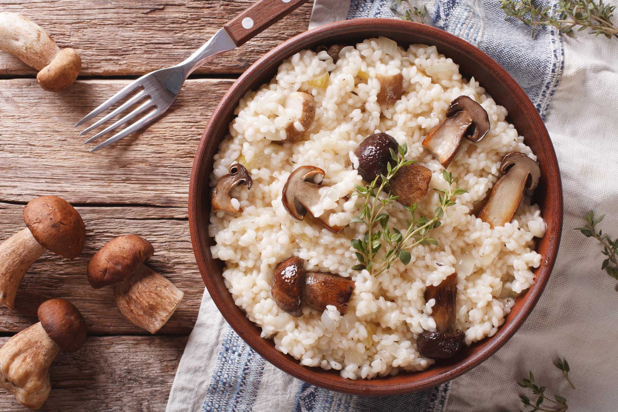 Bowl of risotto with sliced mushrooms and herbs on wooden table.