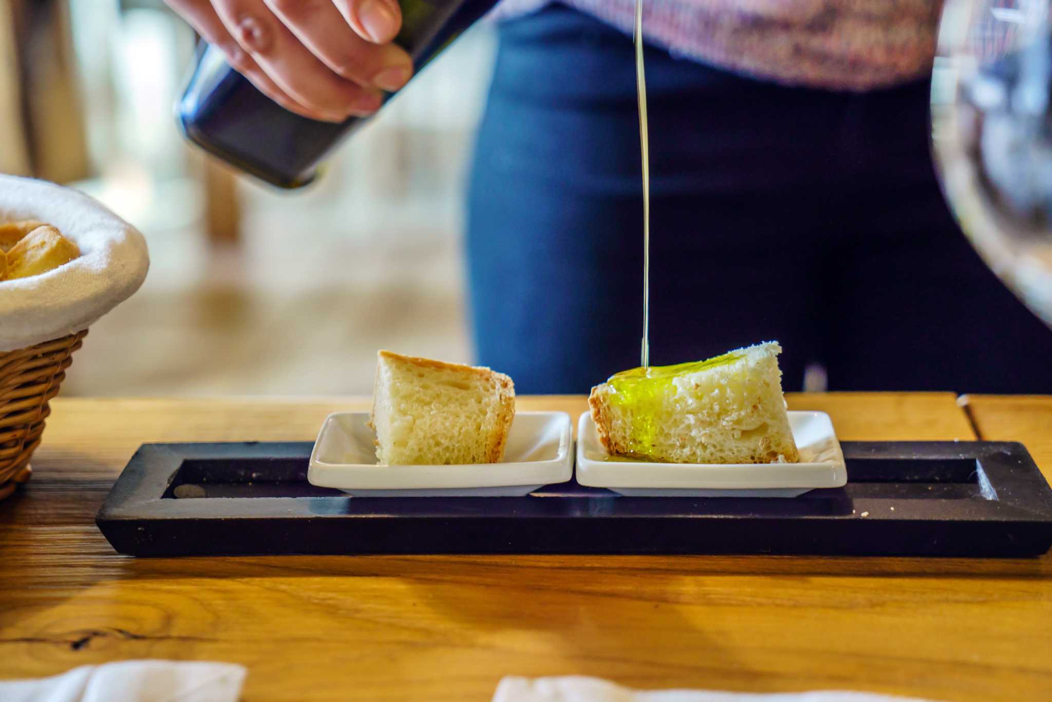 Hand pouring fresh olive oil onto two small plates of bread.
