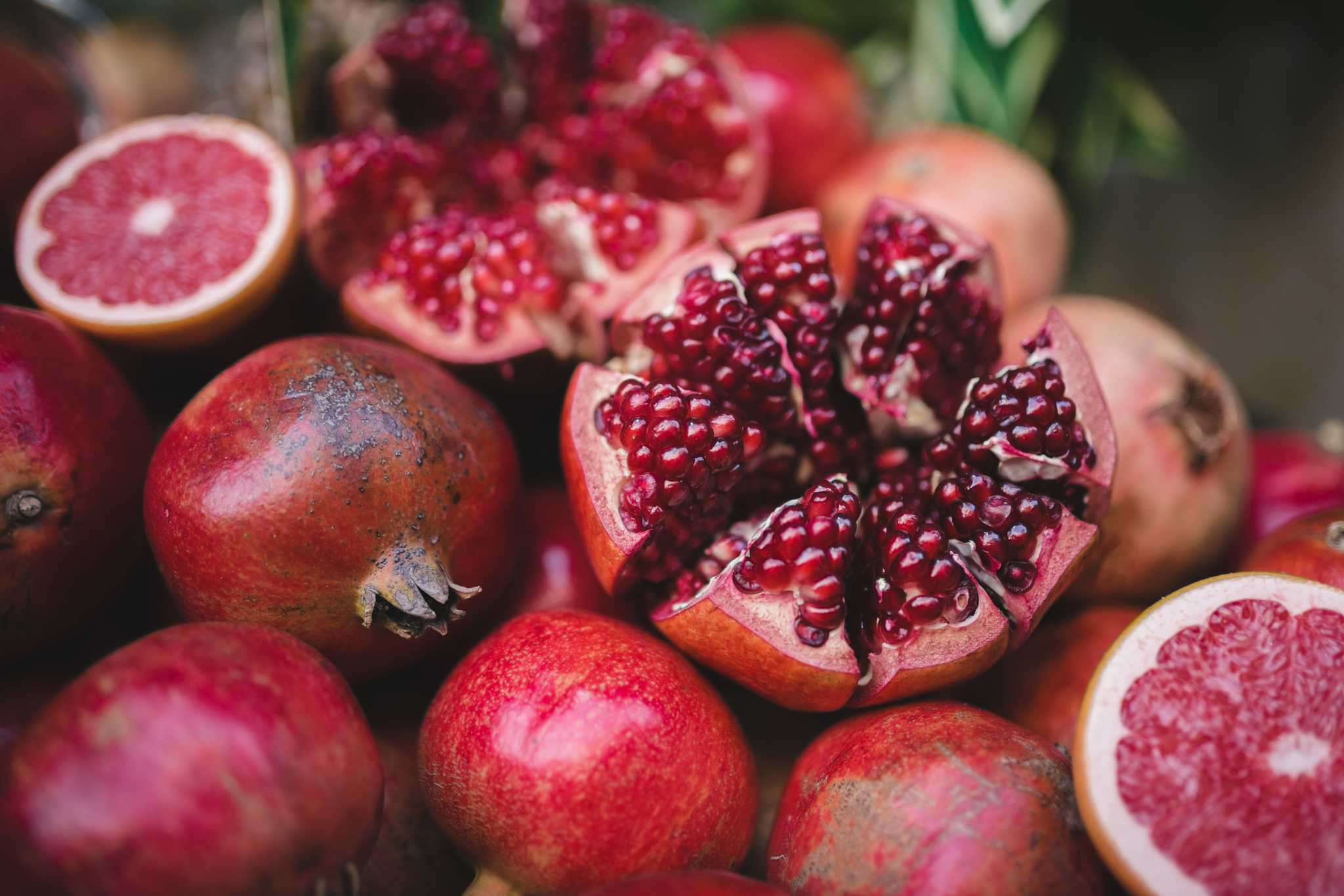 Pile of pomegranates with one cut open, exposing the bright red seeds.