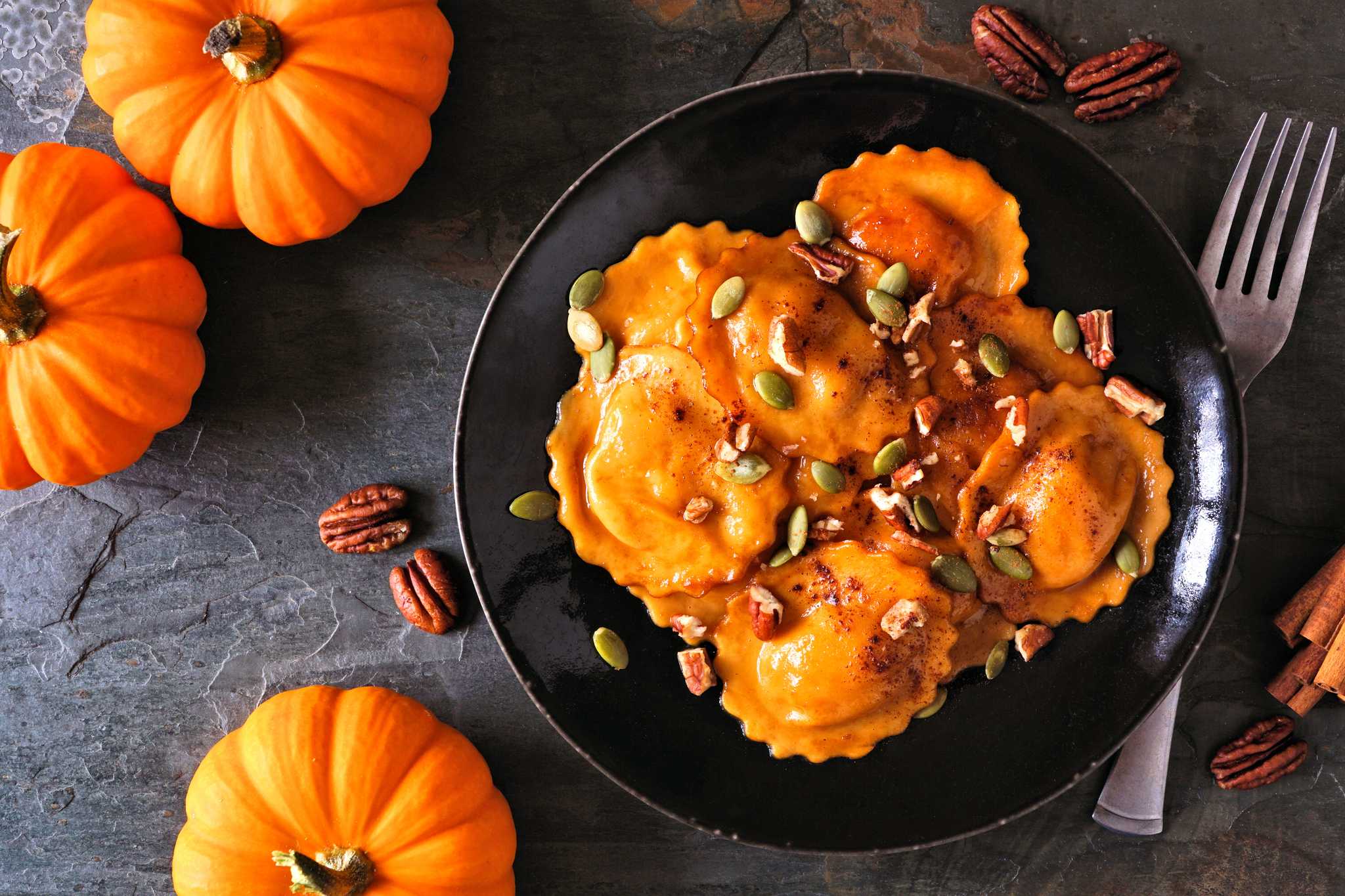 Bowl of pumpkin ravioli on a dark table surrounded by small pumpkins.
