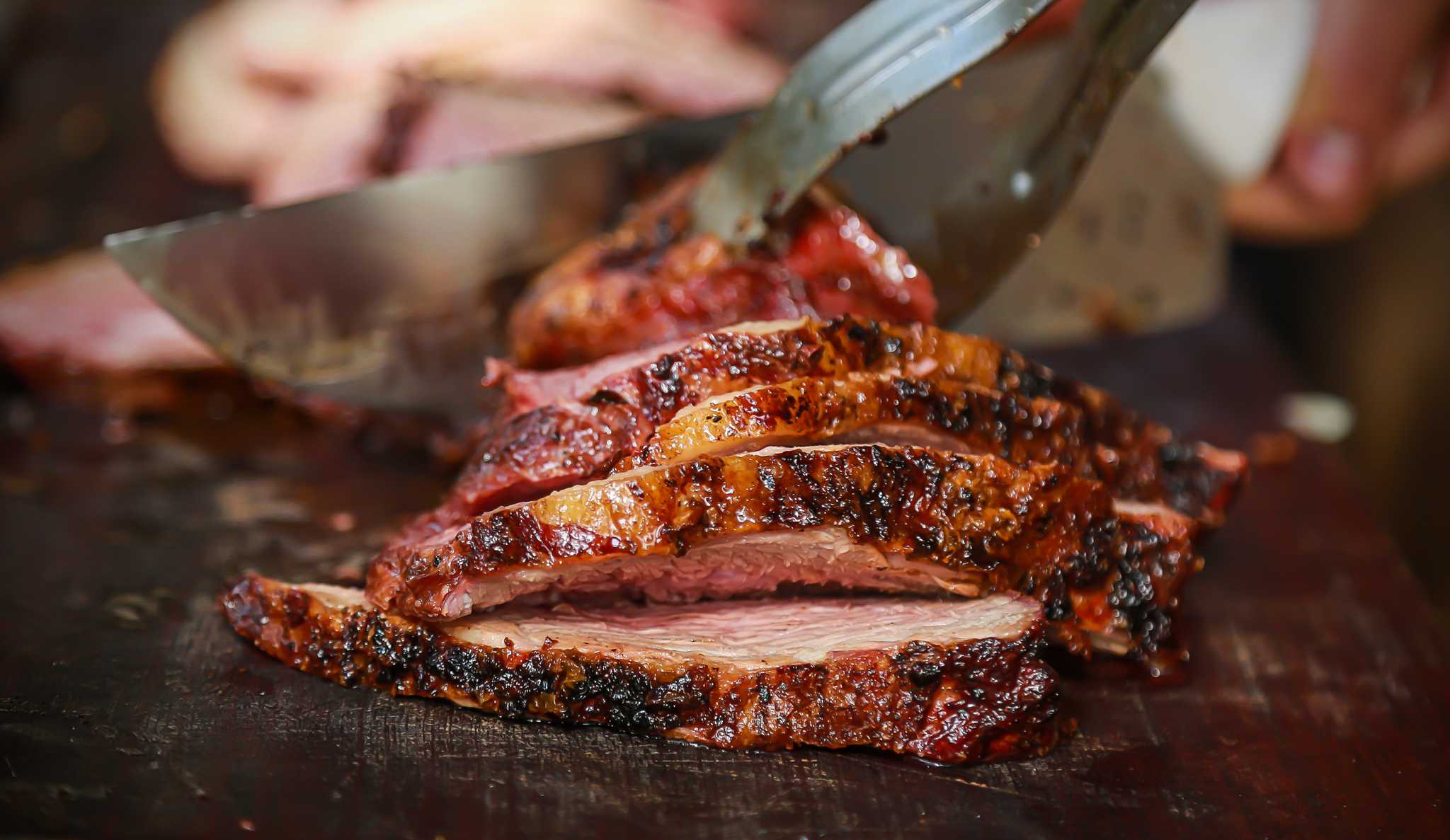 sliced barbacoa meat being handled with tongs on a wooden cutting board.
