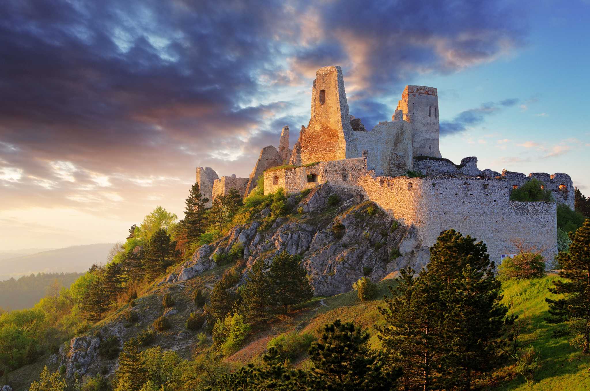 The ruins of Bathory Castle on a hill, with warm sunset light on one side.