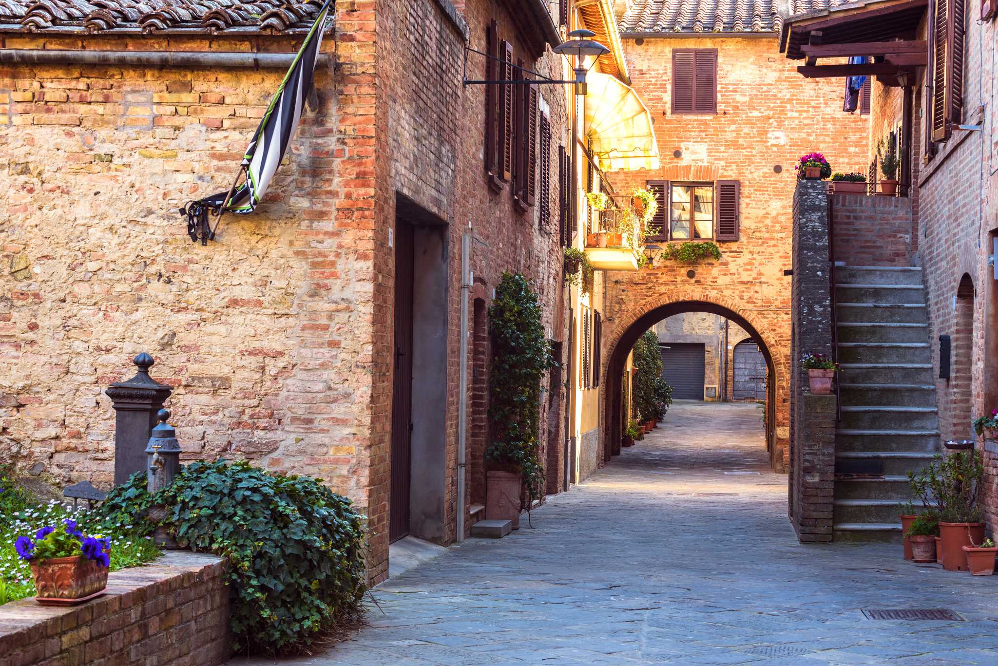 Quiet brick-lined lane with potted plants, stone steps, and an archway.
