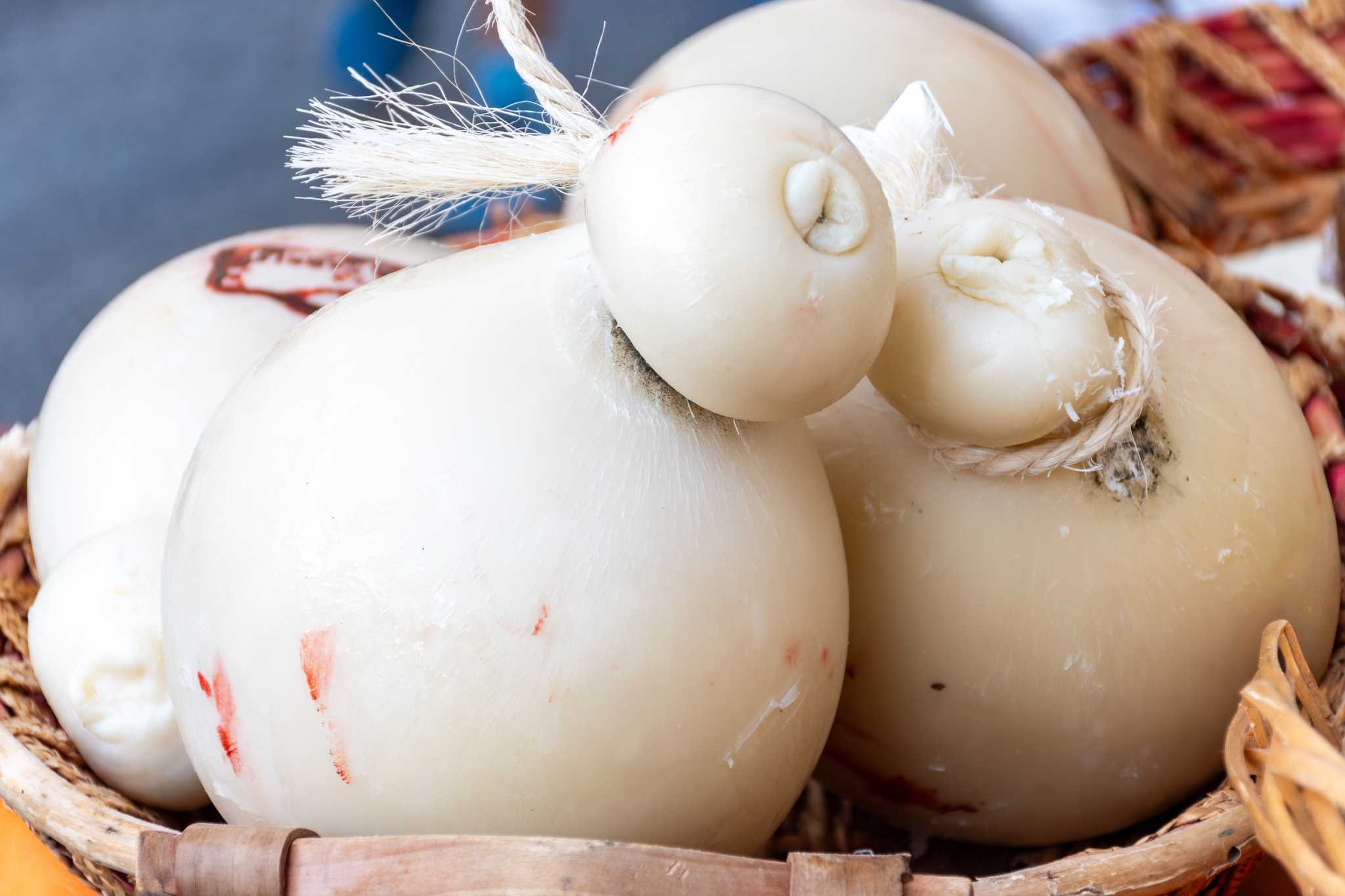A close-up of several whole caciocavallo cheeses in a woven basket.