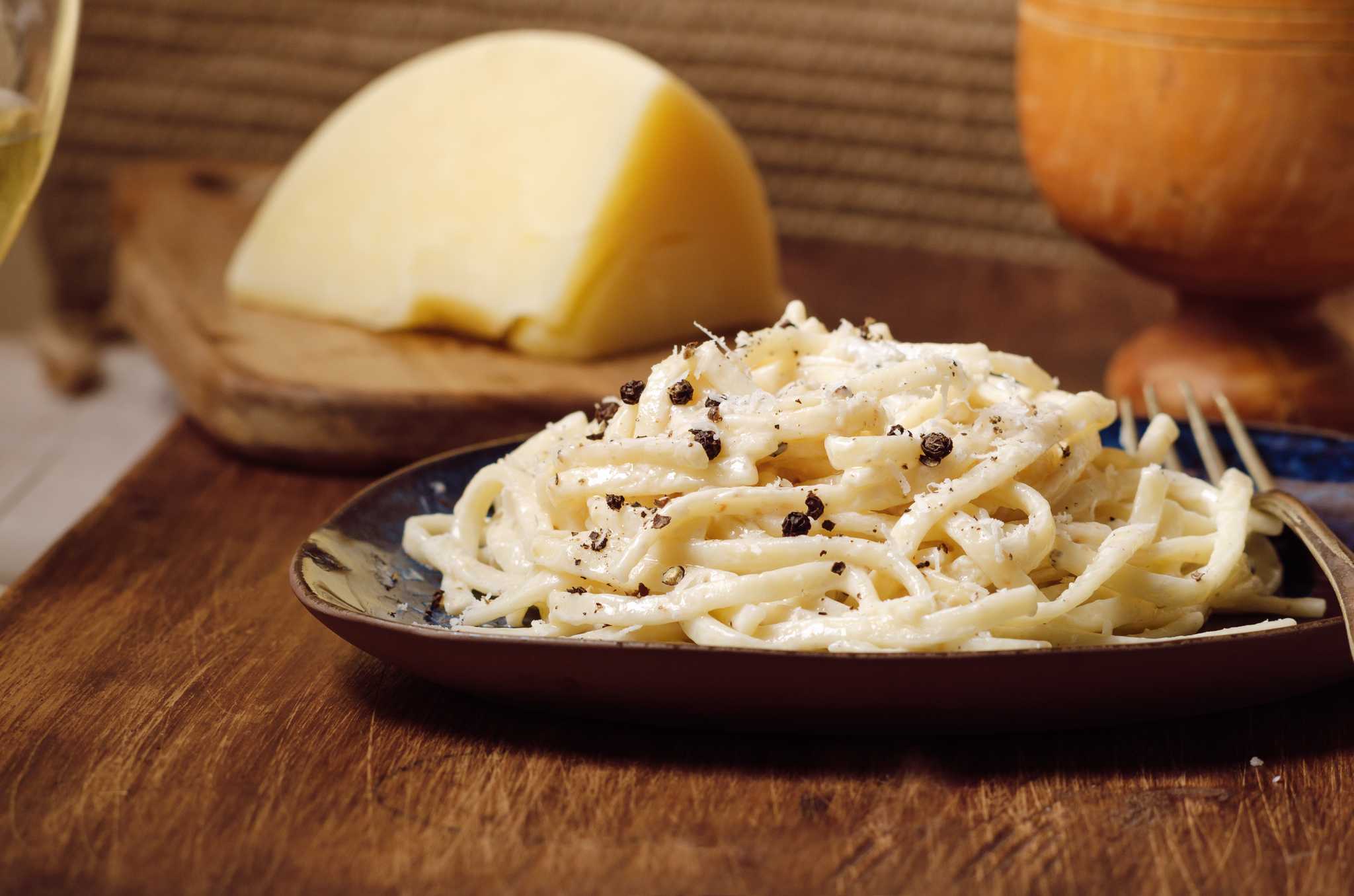 A plate of Italian pasta with grated Pecorino Romano cheese and black pepper on a wooden cutting board.