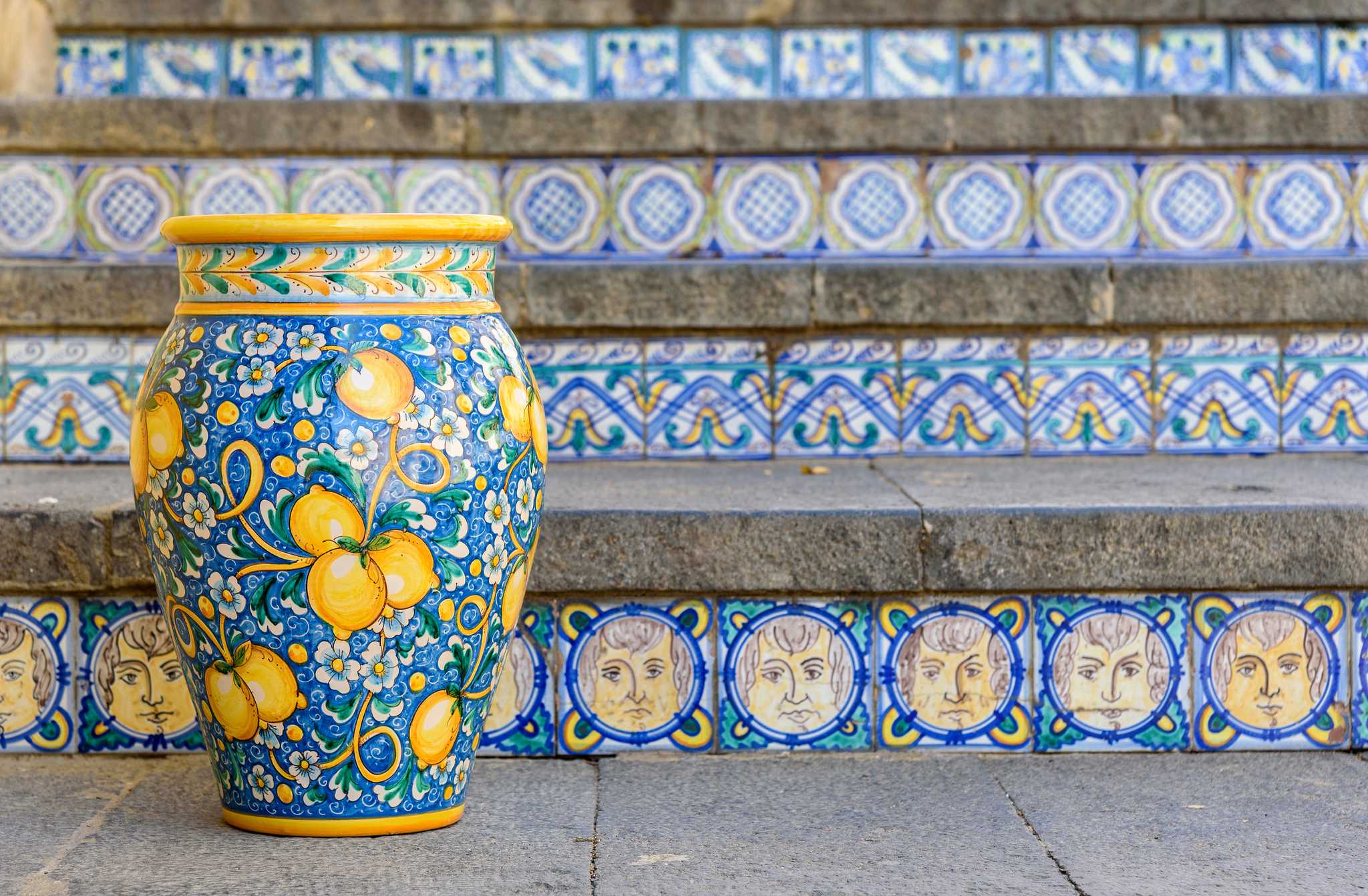 Hand-painted ceramic vase on tiled steps decorated with blue and yellow patterns.