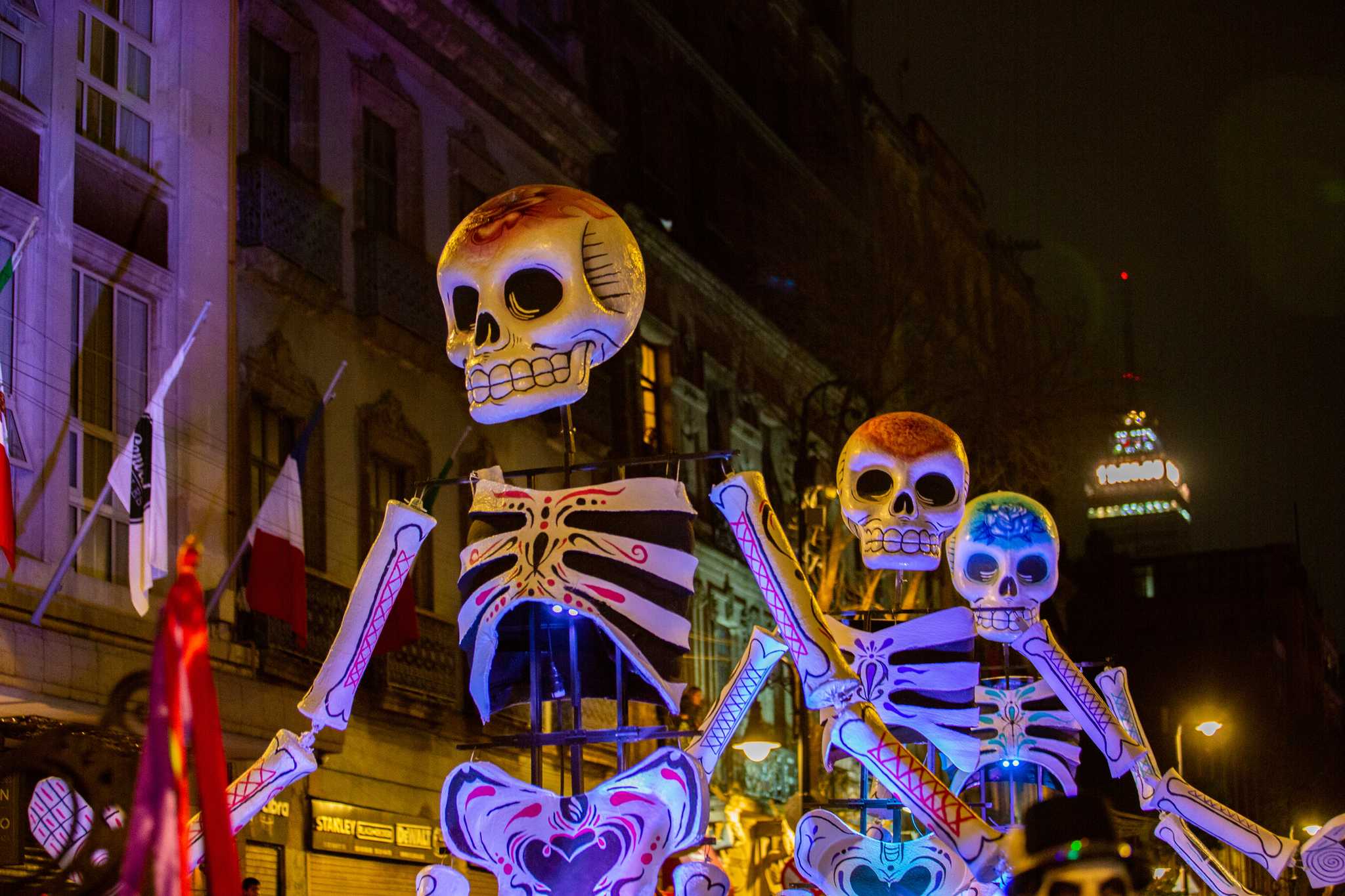 Giant painted skeleton figures parade through Mexico City’s historic center at night.