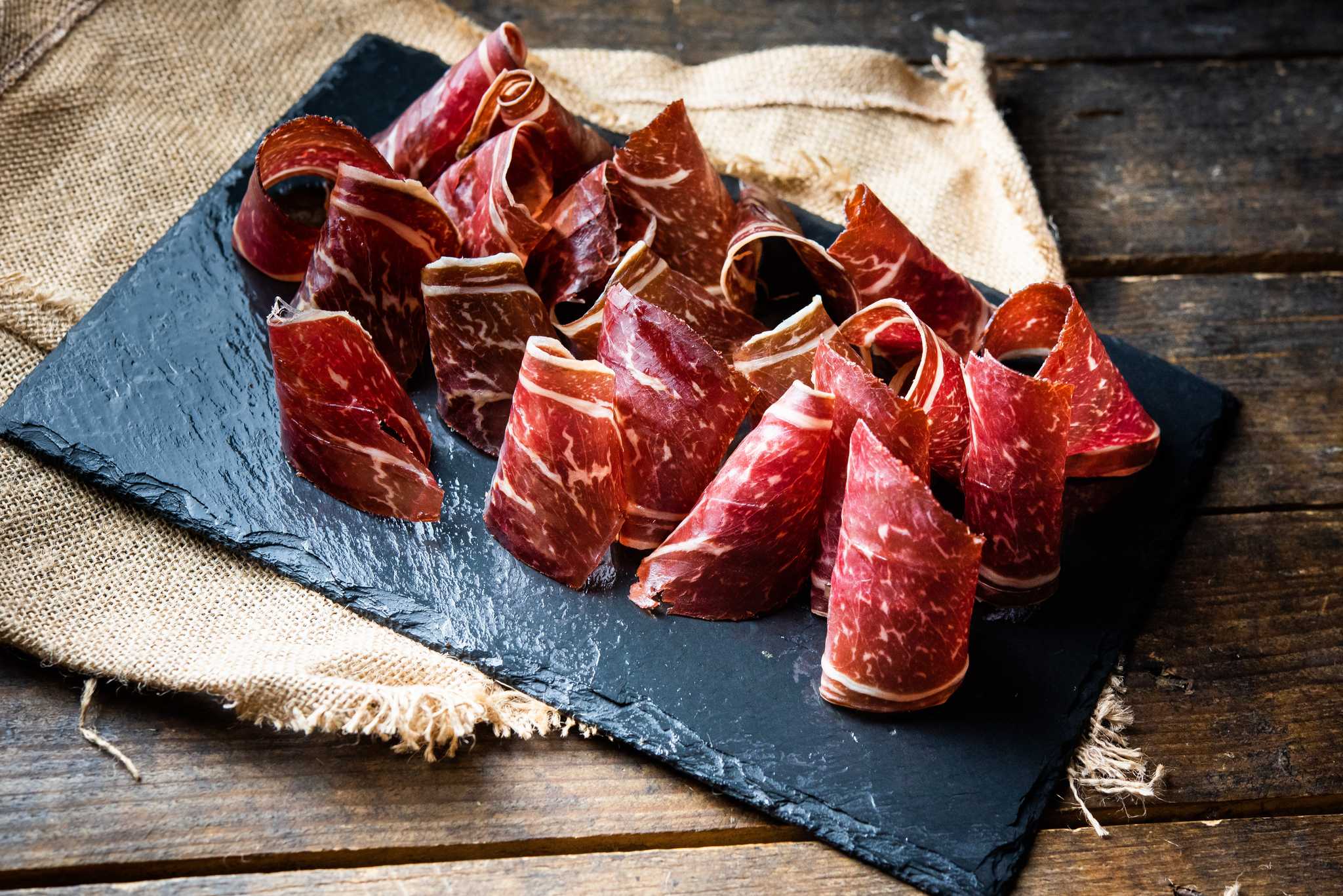 thinly sliced and dried beef strips neatly displayed on a slate board.