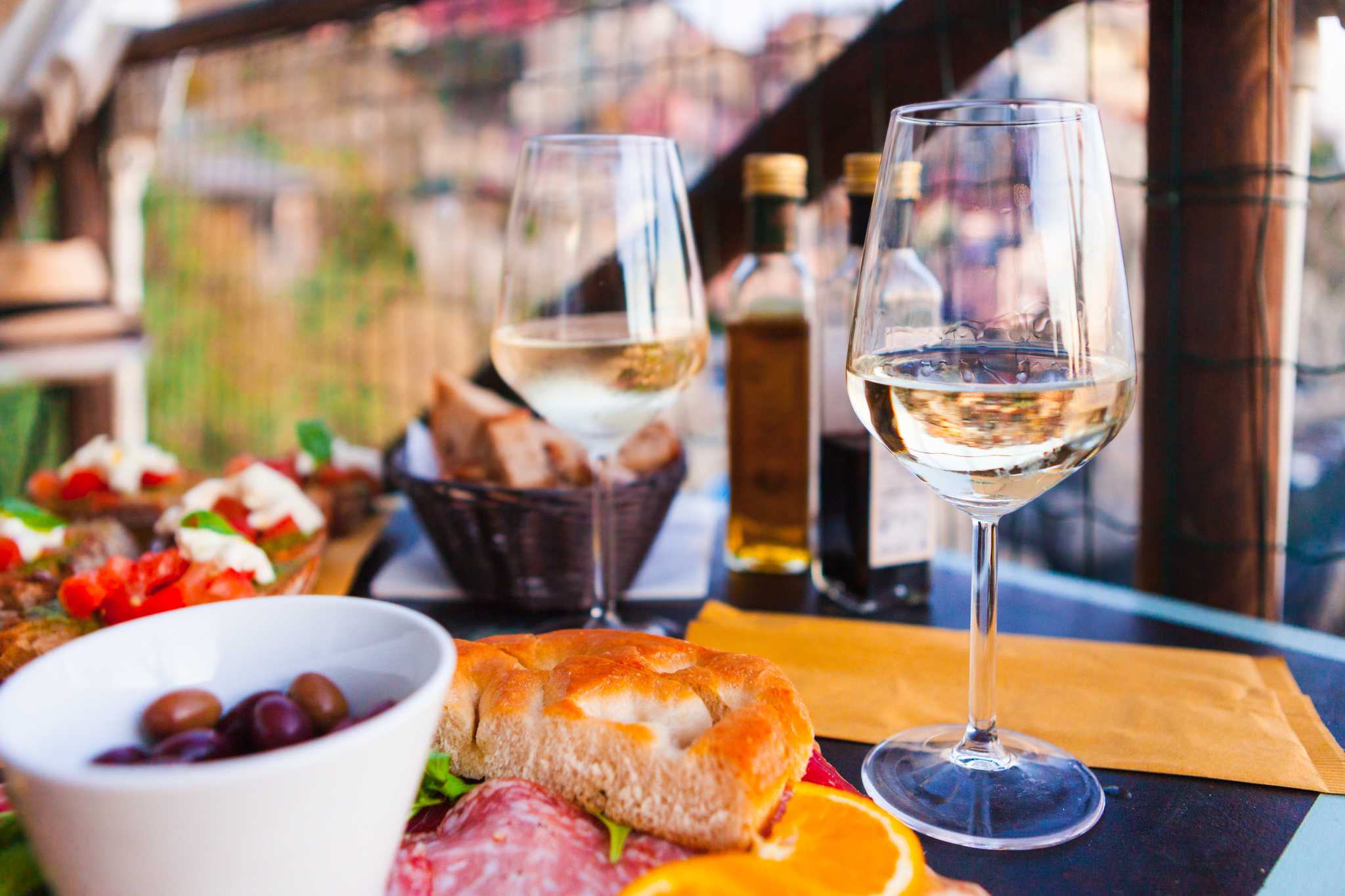 Glasses of white wine with olives, bread, and cured meats on a table.